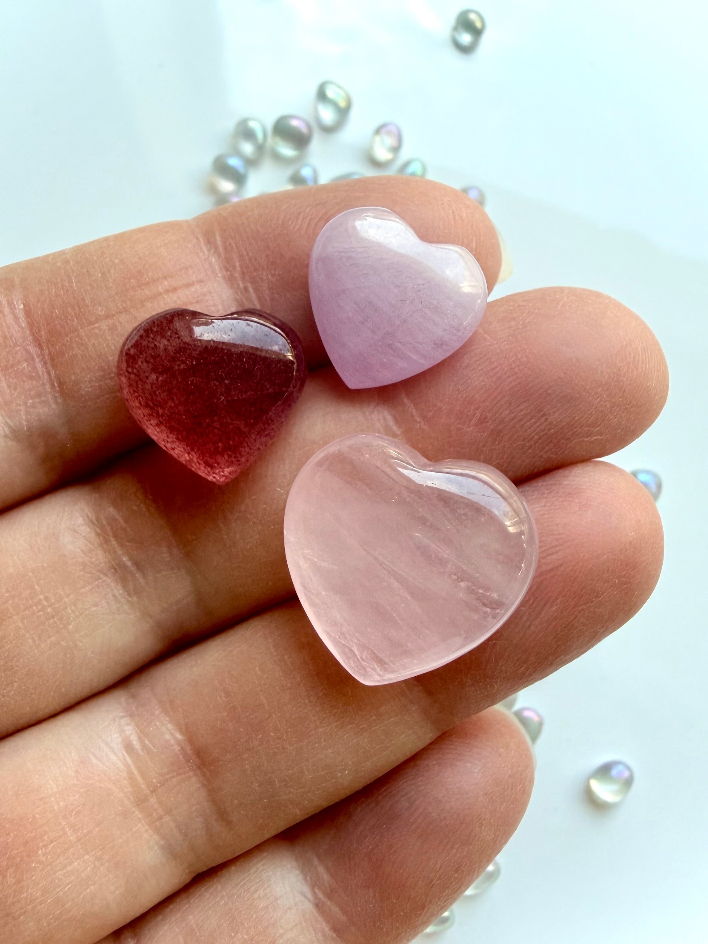 Mini crystal heart trio in hand showing size of rose quartz, strawberry quartz, and kunzite pocket stones