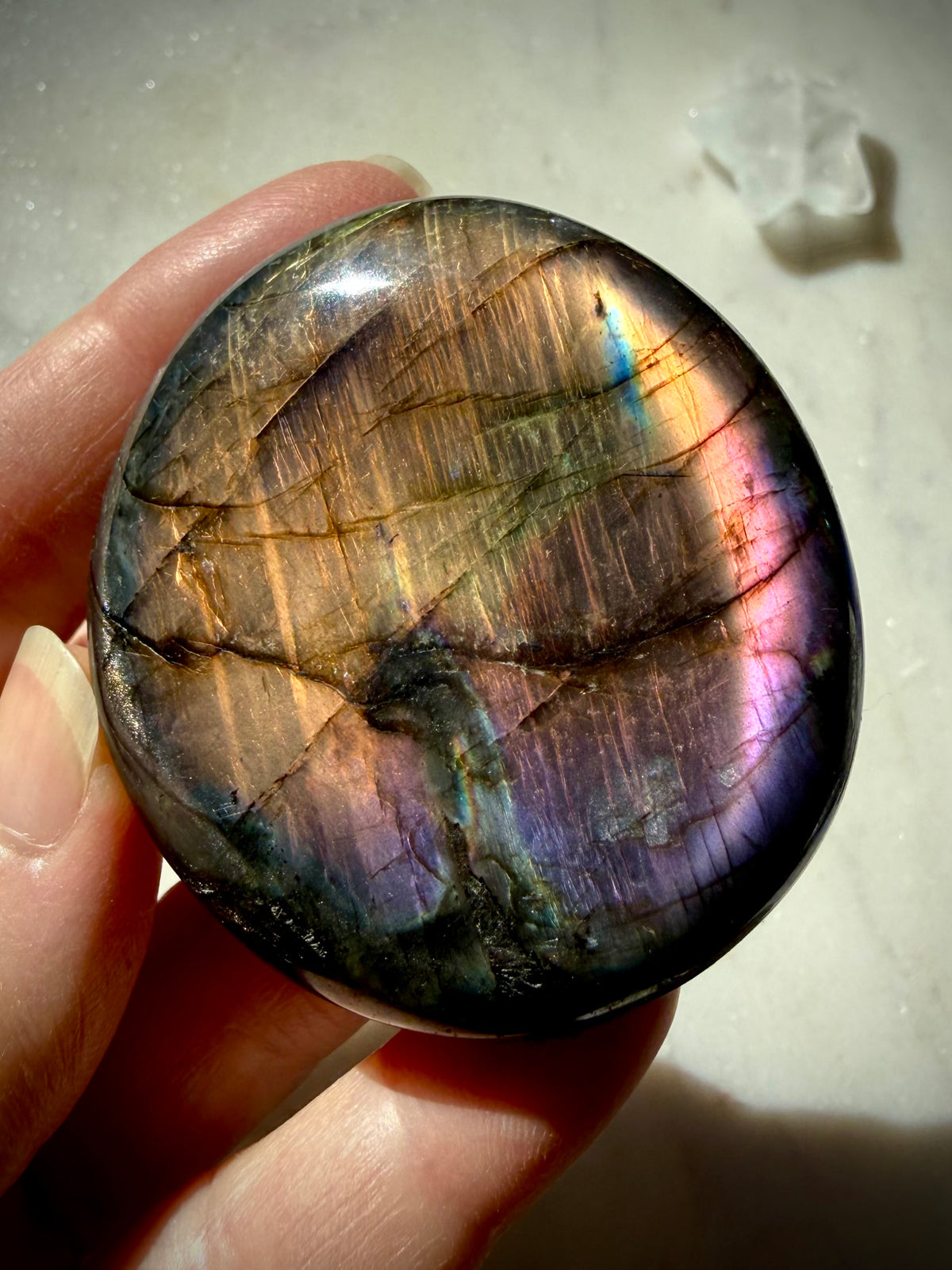 Rainbow Labradorite palm stone held in hand with luminous gold, green, pink and purple flash across the polished surface