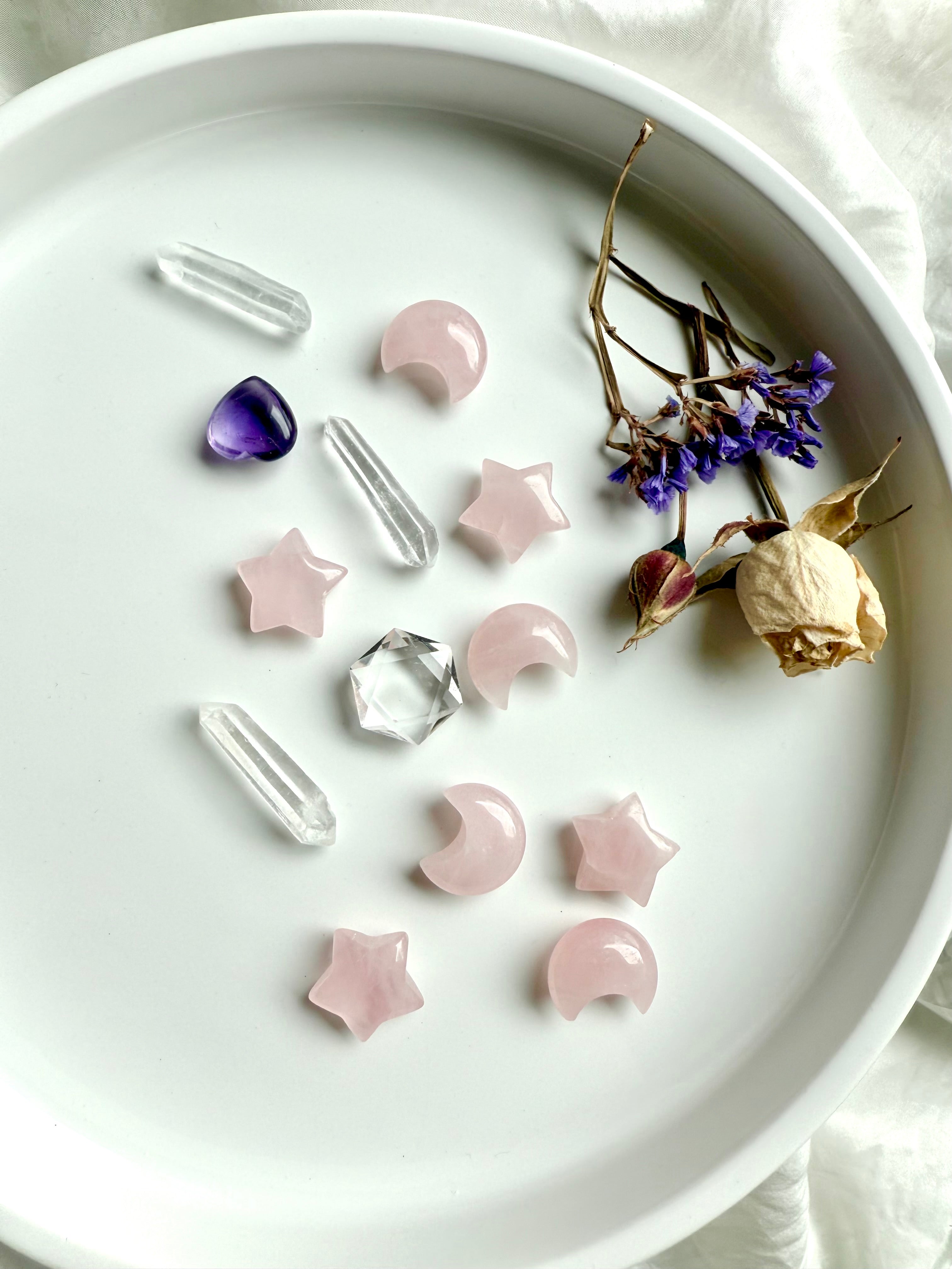 Lifestyle view of mini Rose Quartz carvings styled with quartz points, amethyst heart, clear quartz hexagon, and flowers. Crystal moons and stars for romantic, heart-centered décor and healing crystals.