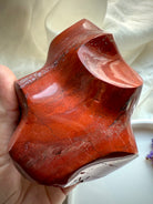 Hand-held Red Ocean Jasper flame with deep red layers, grounding Root Chakra energy, and swirling natural textures.