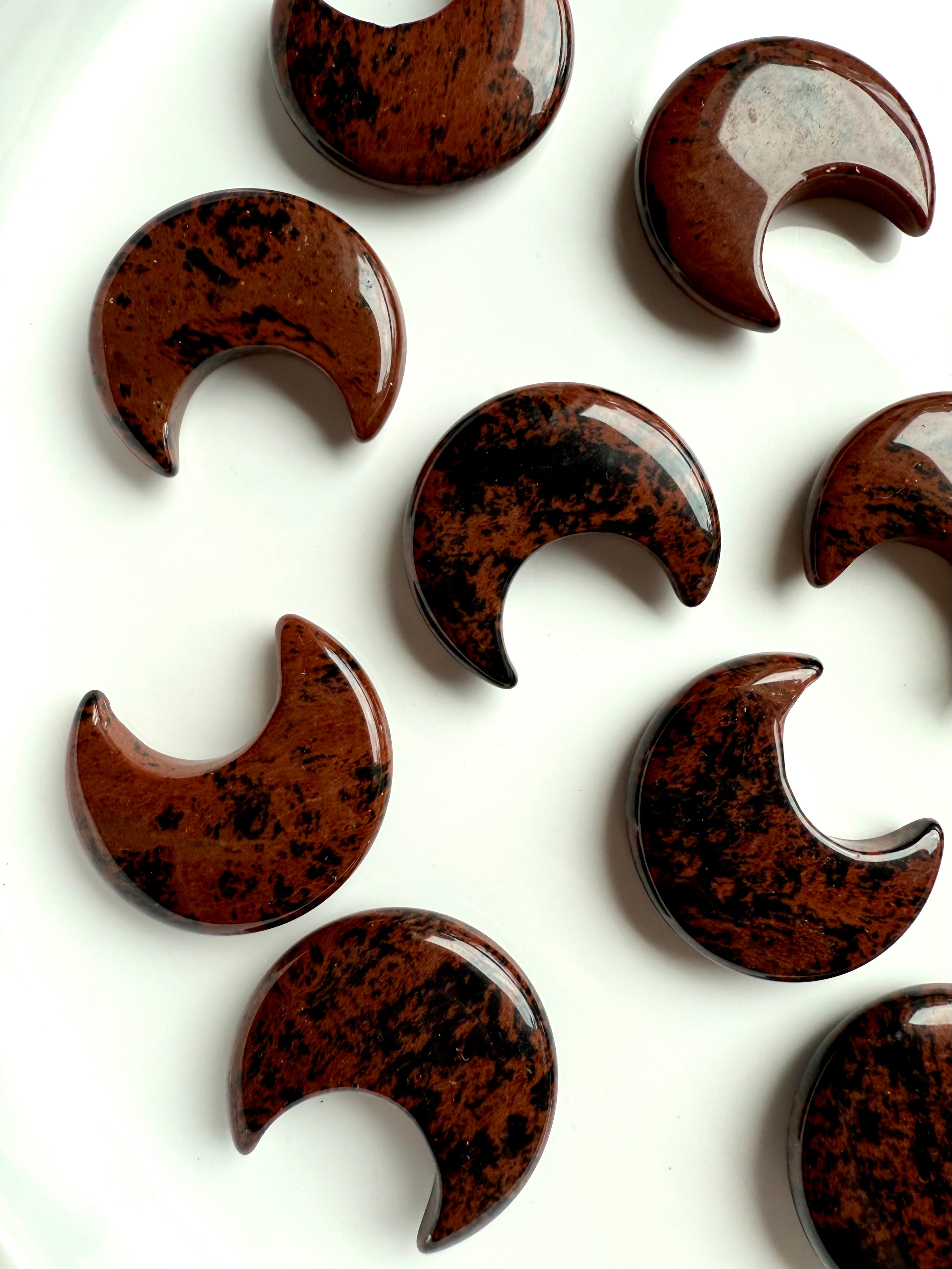 Closeup of high quality Mahogany Obsidian crescent moon carvings displayed on a white plate. 