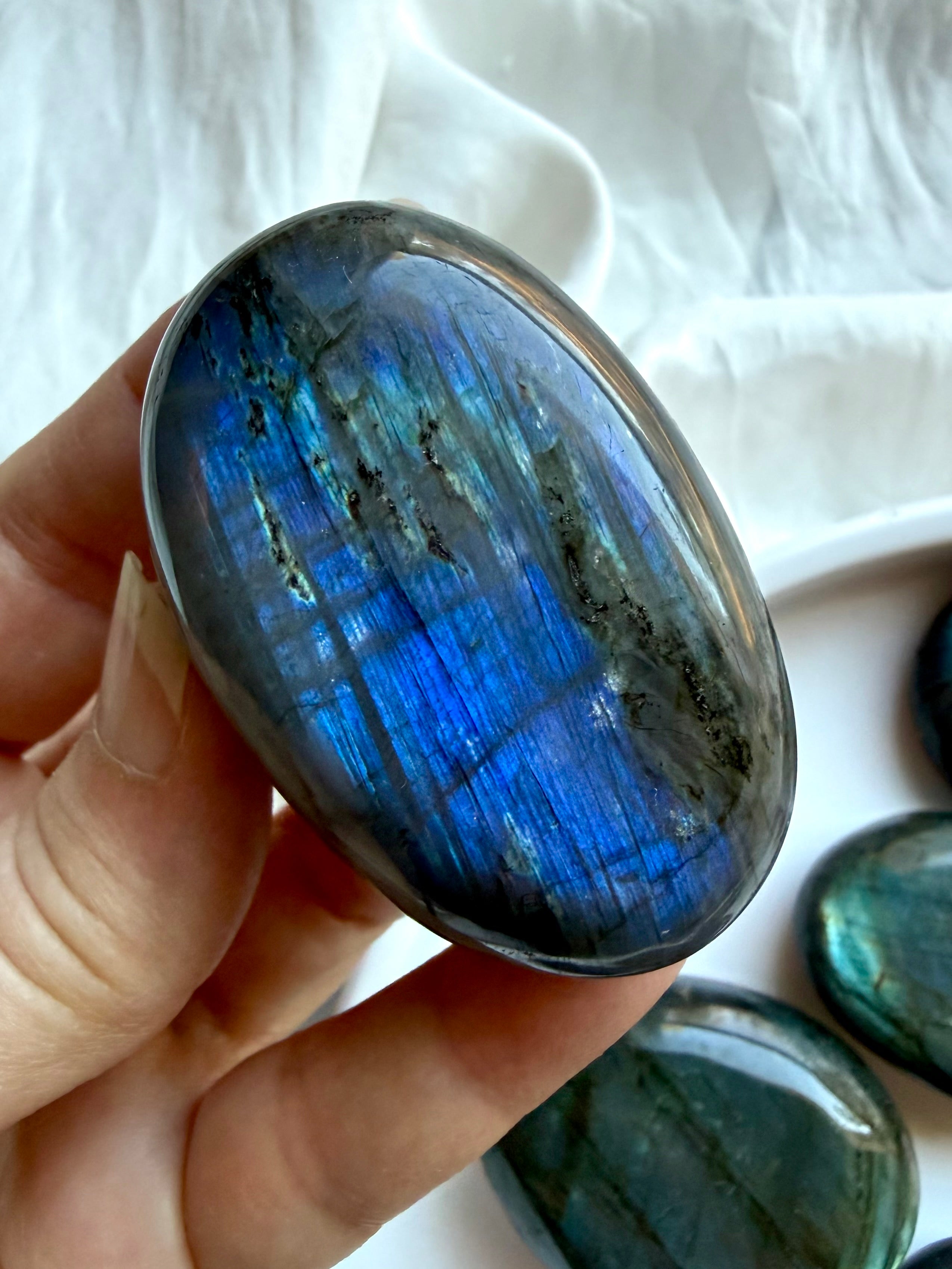 Electric blue Labradorite palm stone held in hand with colorful flash and polished crystal surface