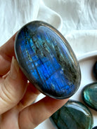 Electric blue Labradorite palm stone held in hand with colorful flash and polished crystal surface