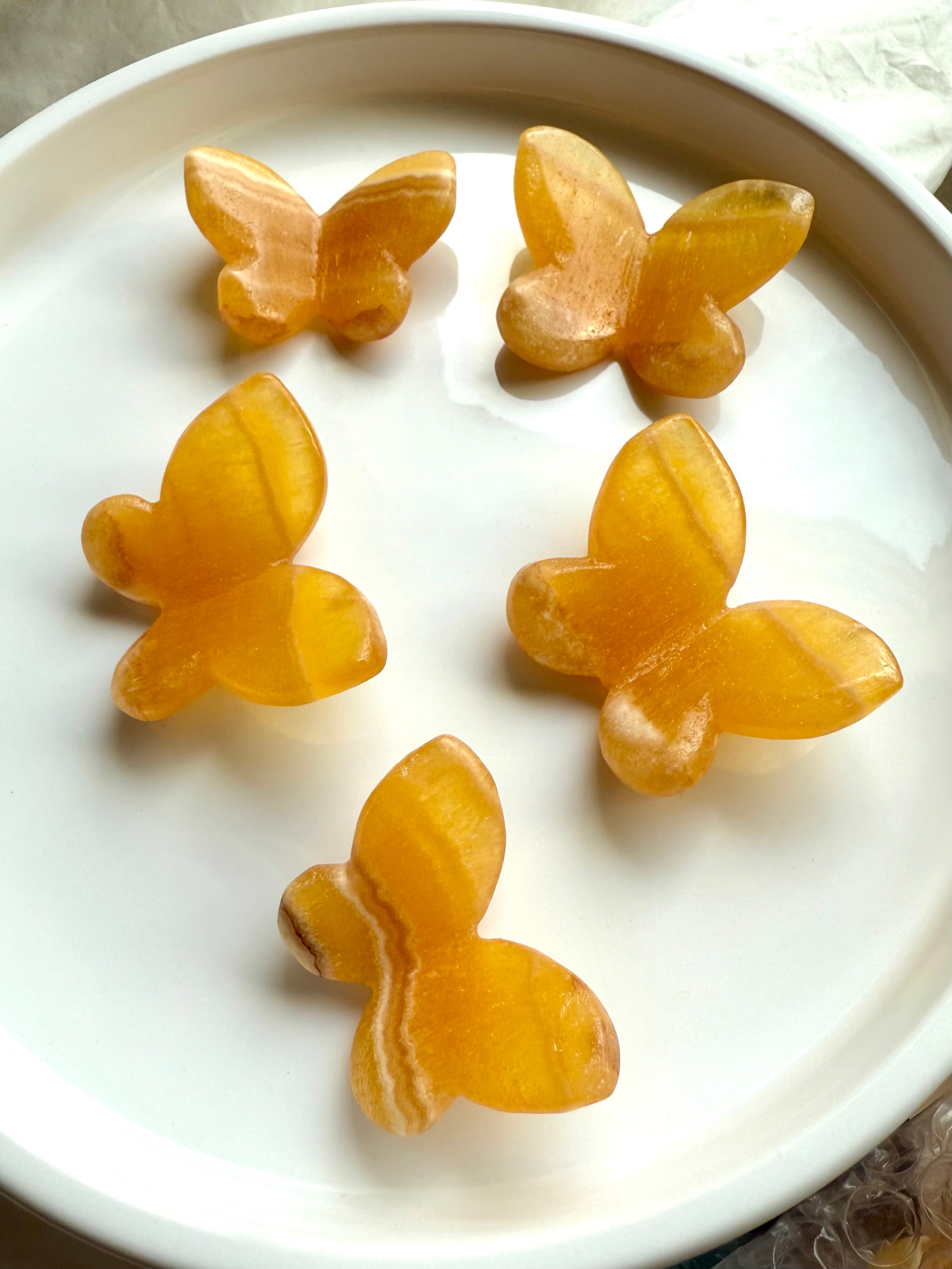 Orange calcite 3d butterfly carvings on a white plate - sacral chakra and solar plexus chakra crystals for joy.