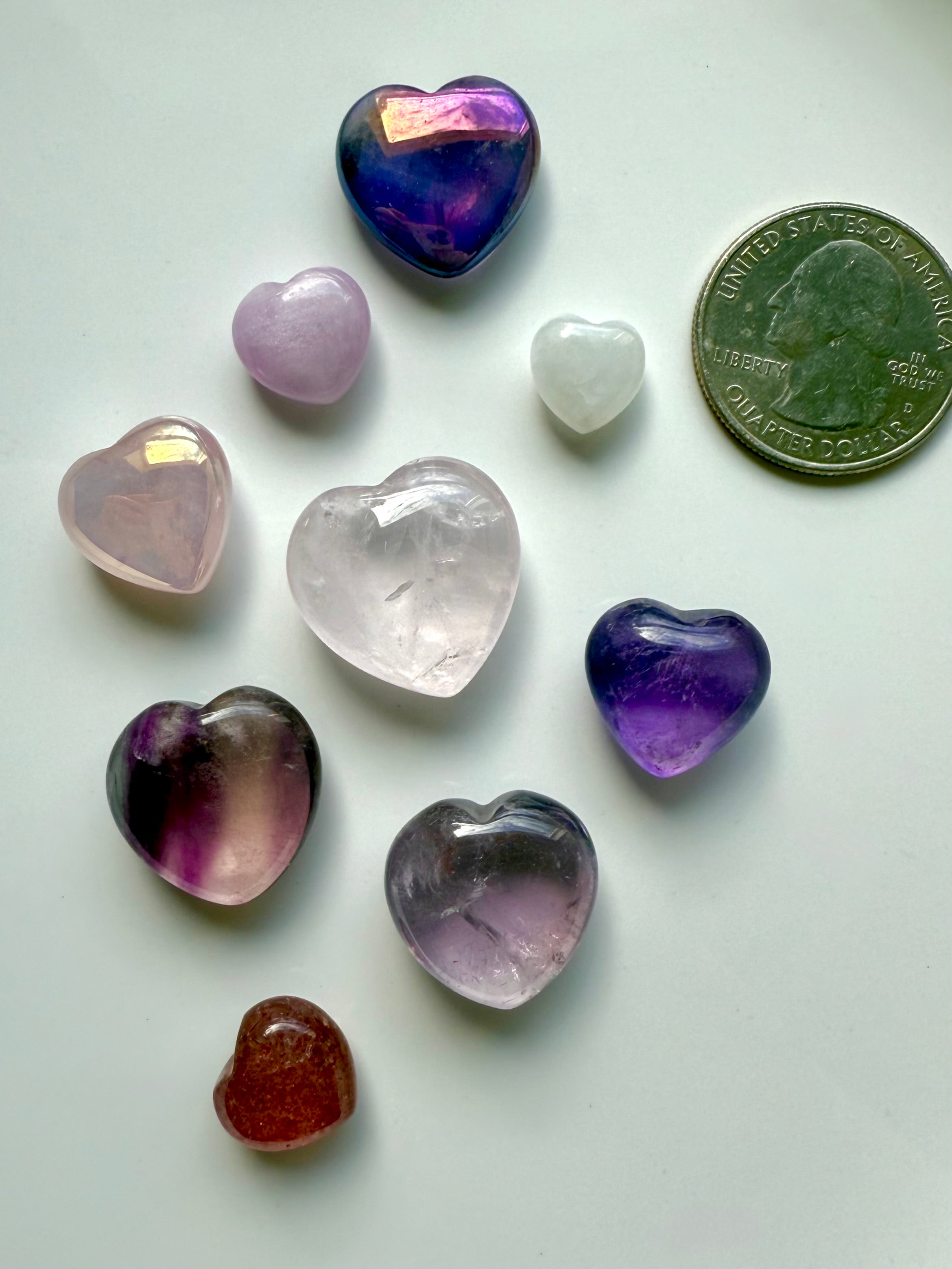 Close-up of pink and purple mini crystal hearts on white background with a quarter for size comparison, premium gemstone carvings.
