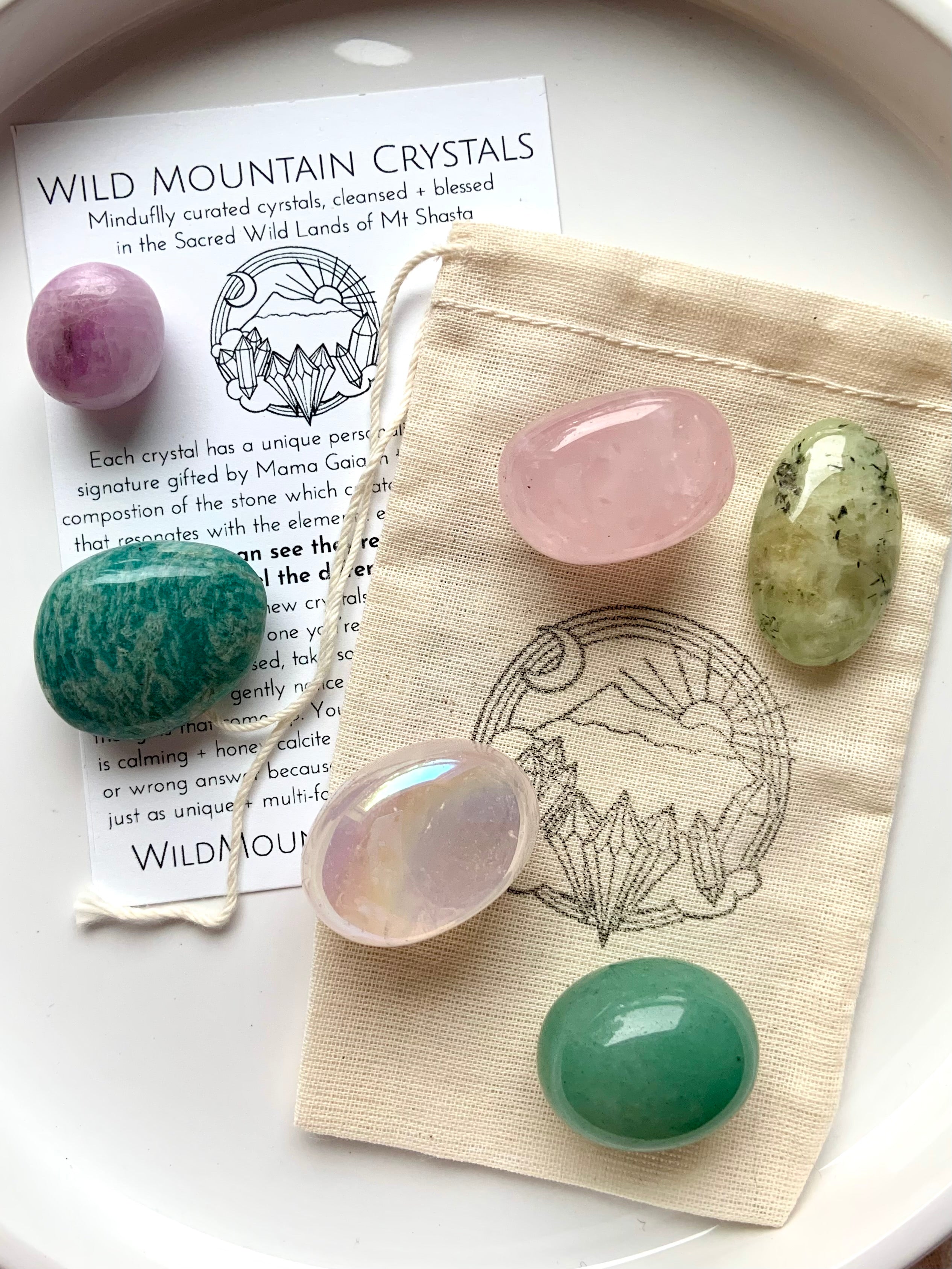 Heart Chakra crystal set on info card and logo pouch — includes aura rose quartz, rose quartz, kunzite, amazonite, green aventurine, and prehnite displayed on a white plate.