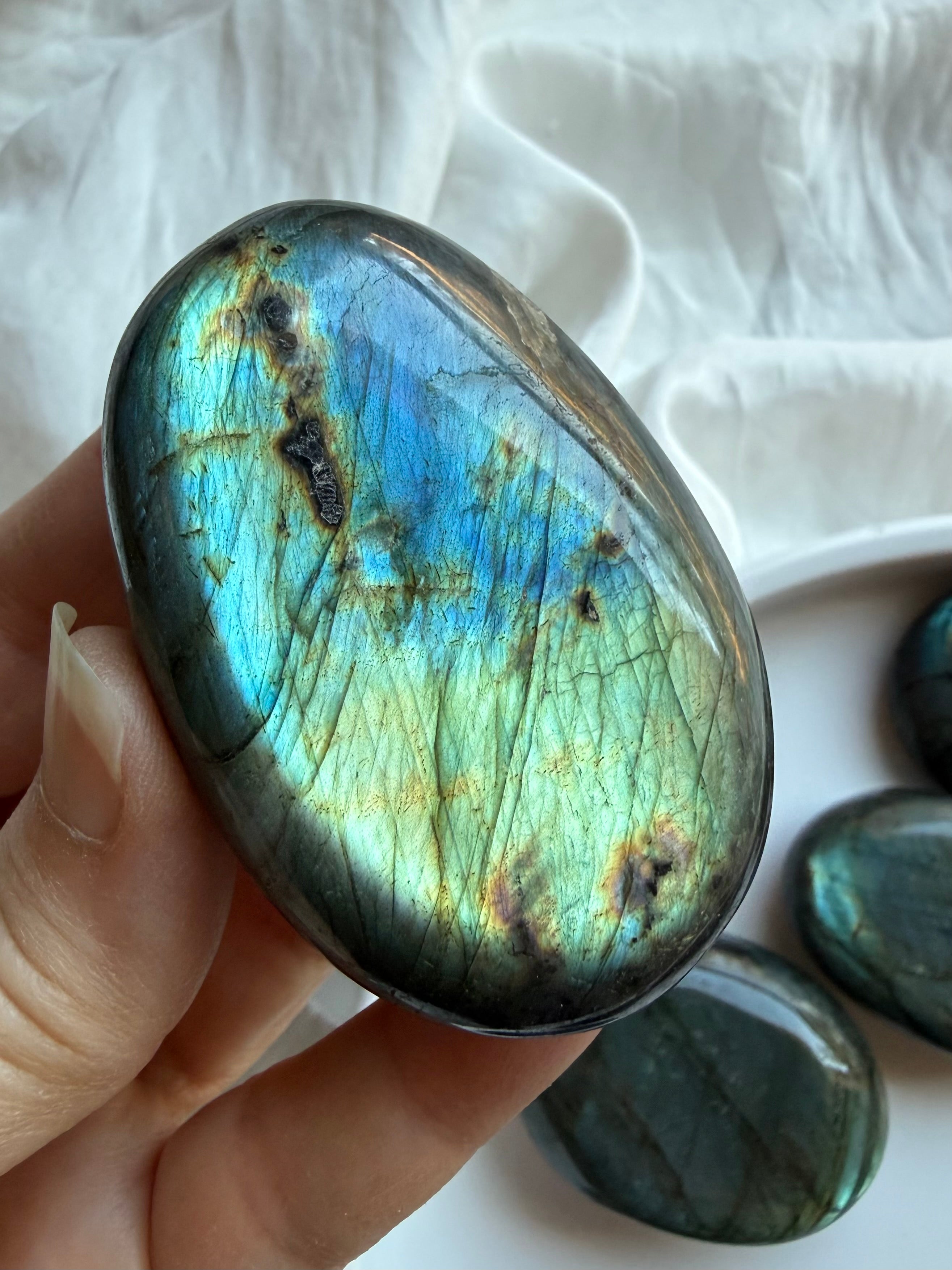 Large Labradorite palm stone held in hand with teal flash and natural black matrix