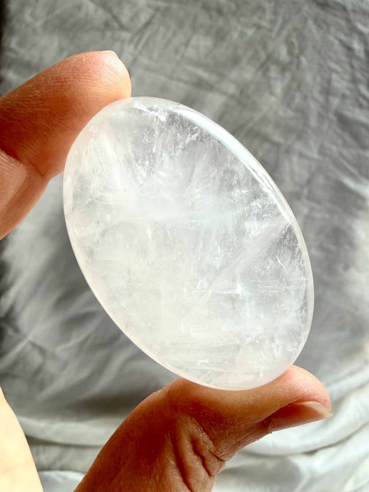 Clear Quartz meditation stone held in hand with luminous white veils, crystalline inclusions and silvery internal reflections