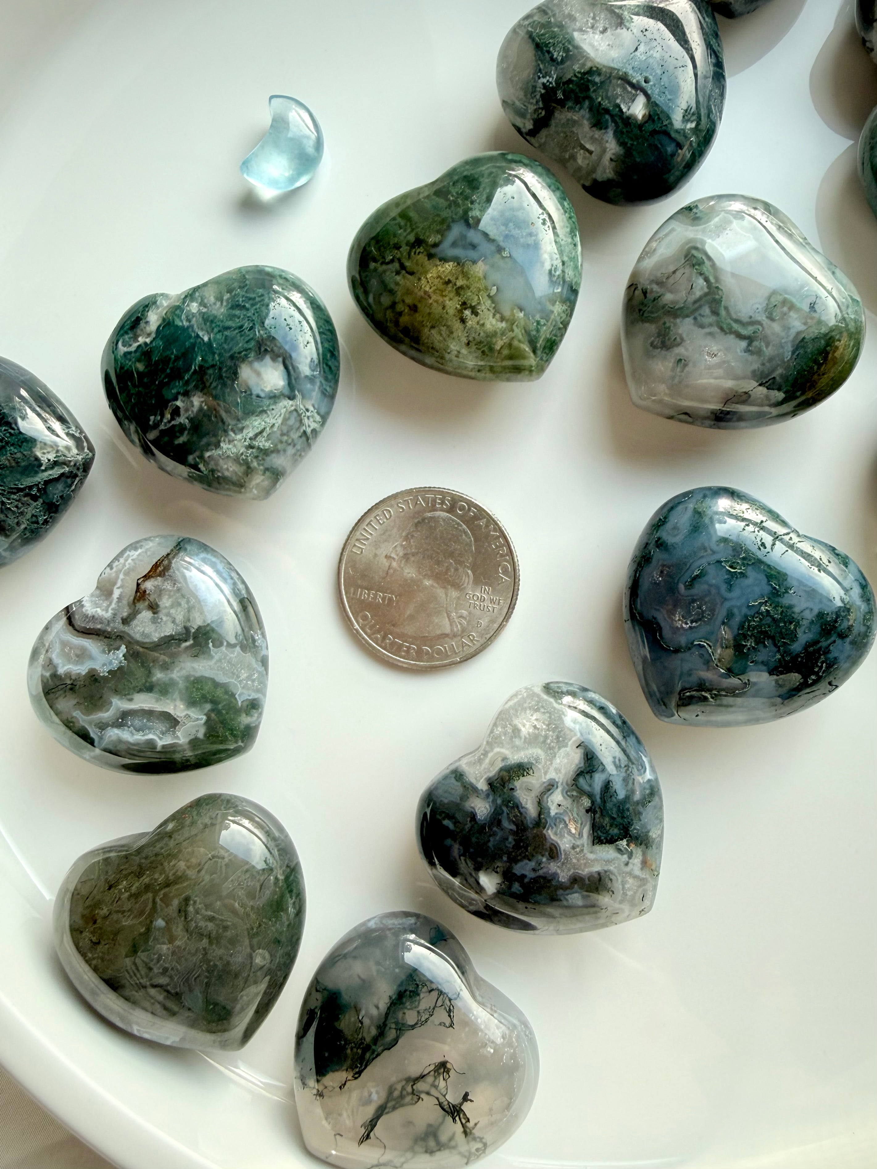 Moss Agate hearts next to a quarter for size reference, showing polished green and grey crystal patterns