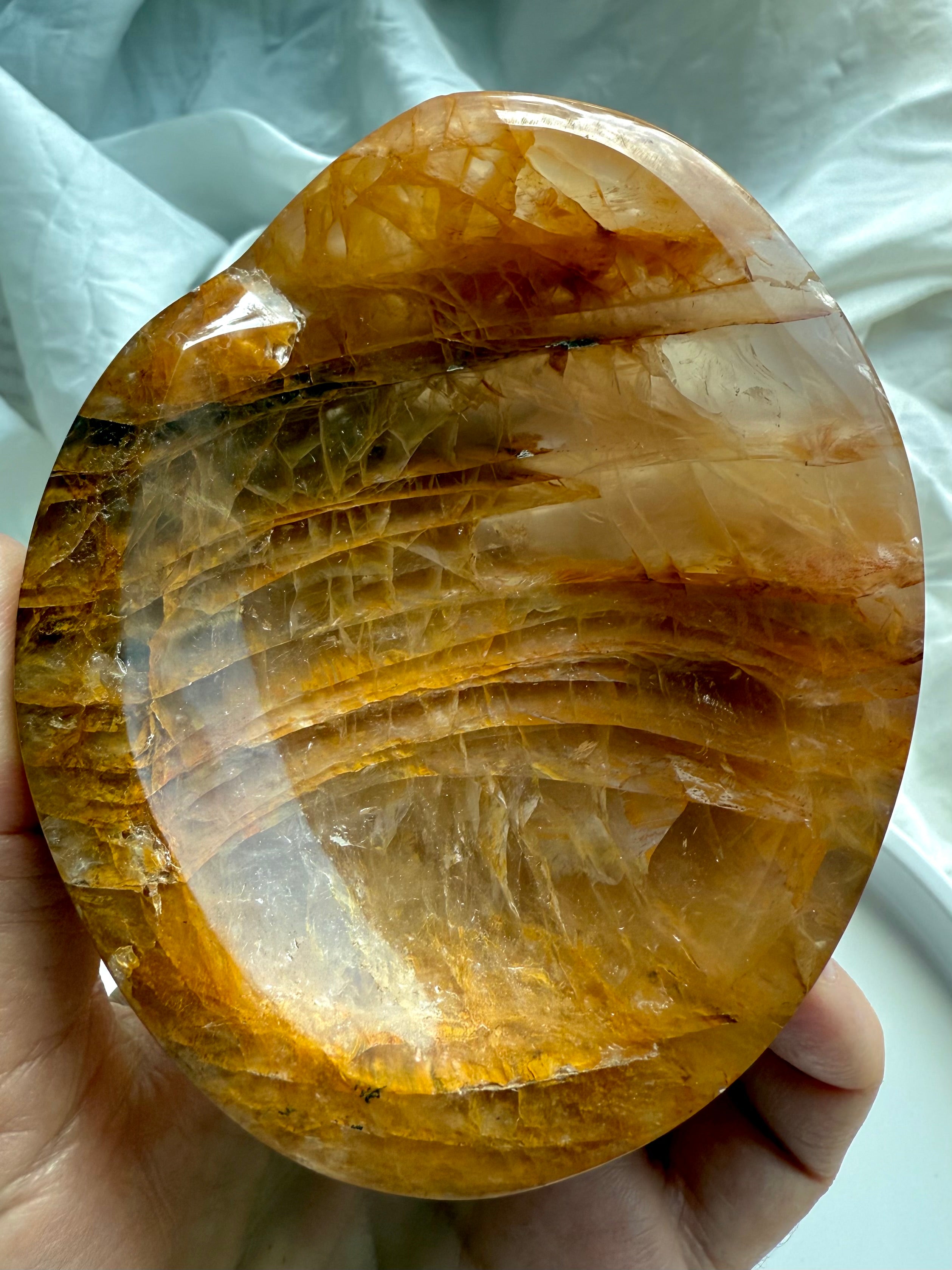 Golden Healer crystal bowl backlit to reveal translucent girasol glow, golden iron inclusions, and unique scooped shape
