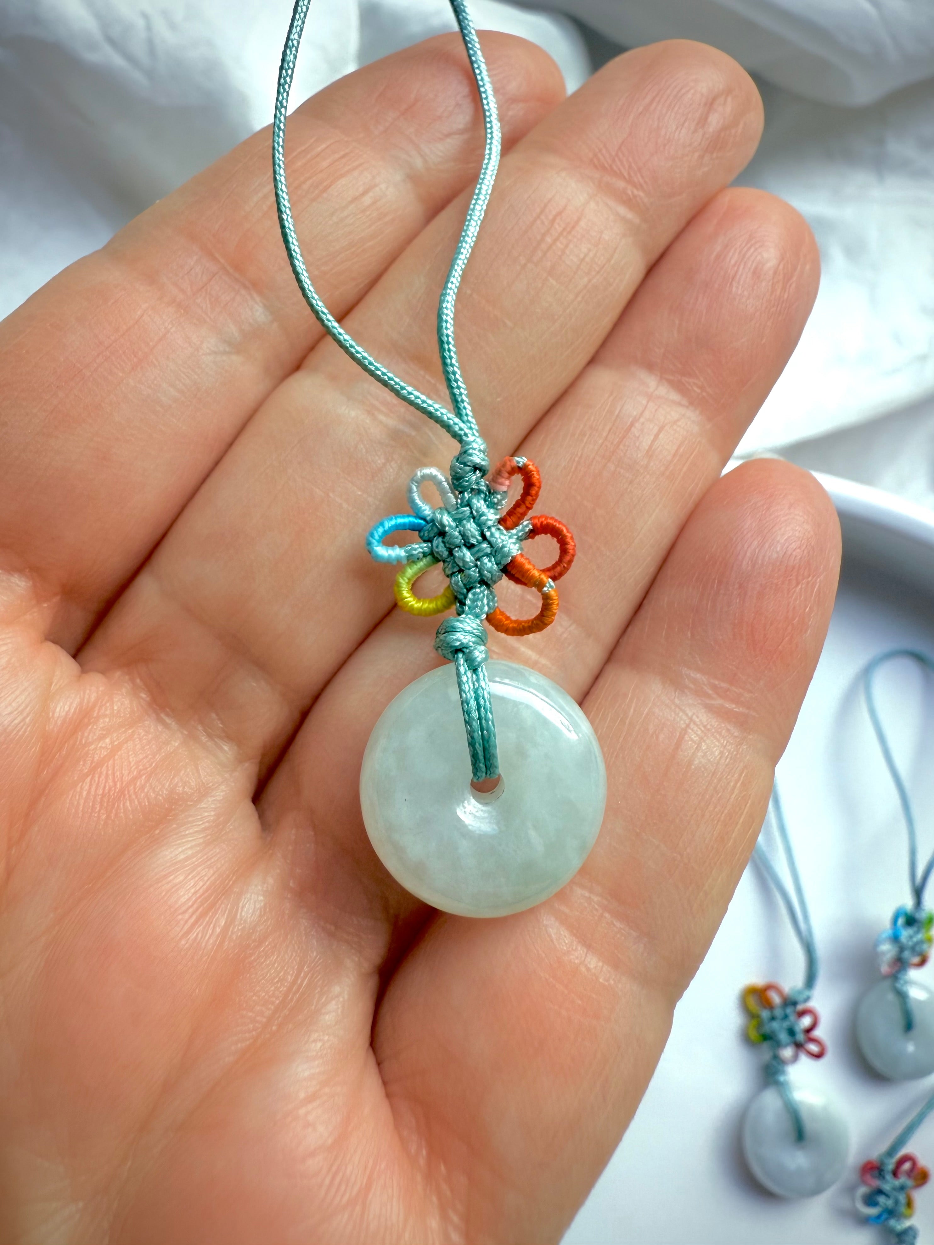 Closeup of hand holding jade peace buckle charm with rainbow lucky knot and satin green cord