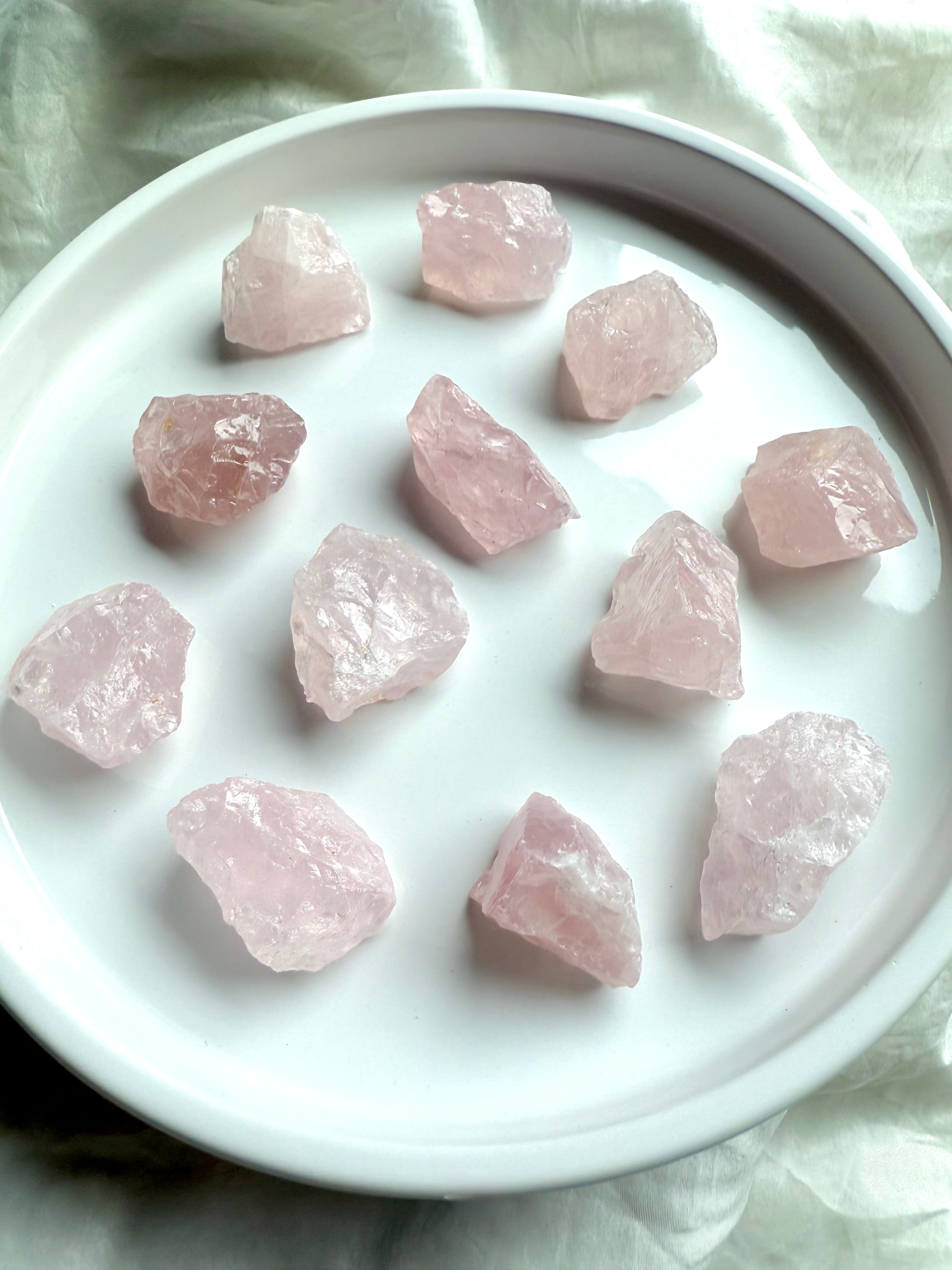 Small raw Rose Quartz chunks with translucent pink color on white. Natural crystals for peace & love.