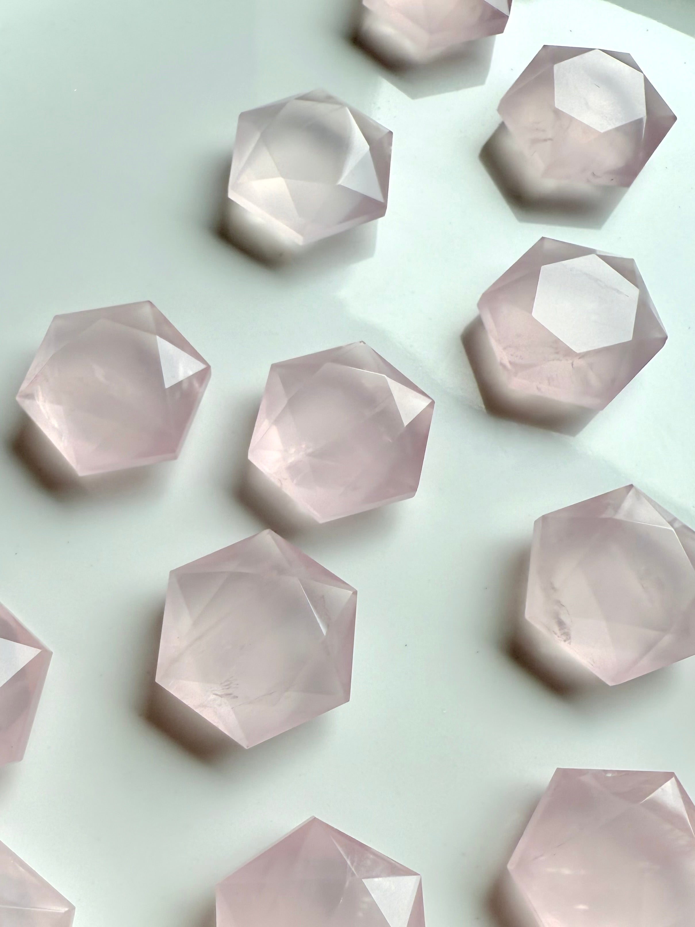 Closeup of mini rose quartz hexagon crystals on white background, translucent pink sacred geometry stones for love, peace & healing