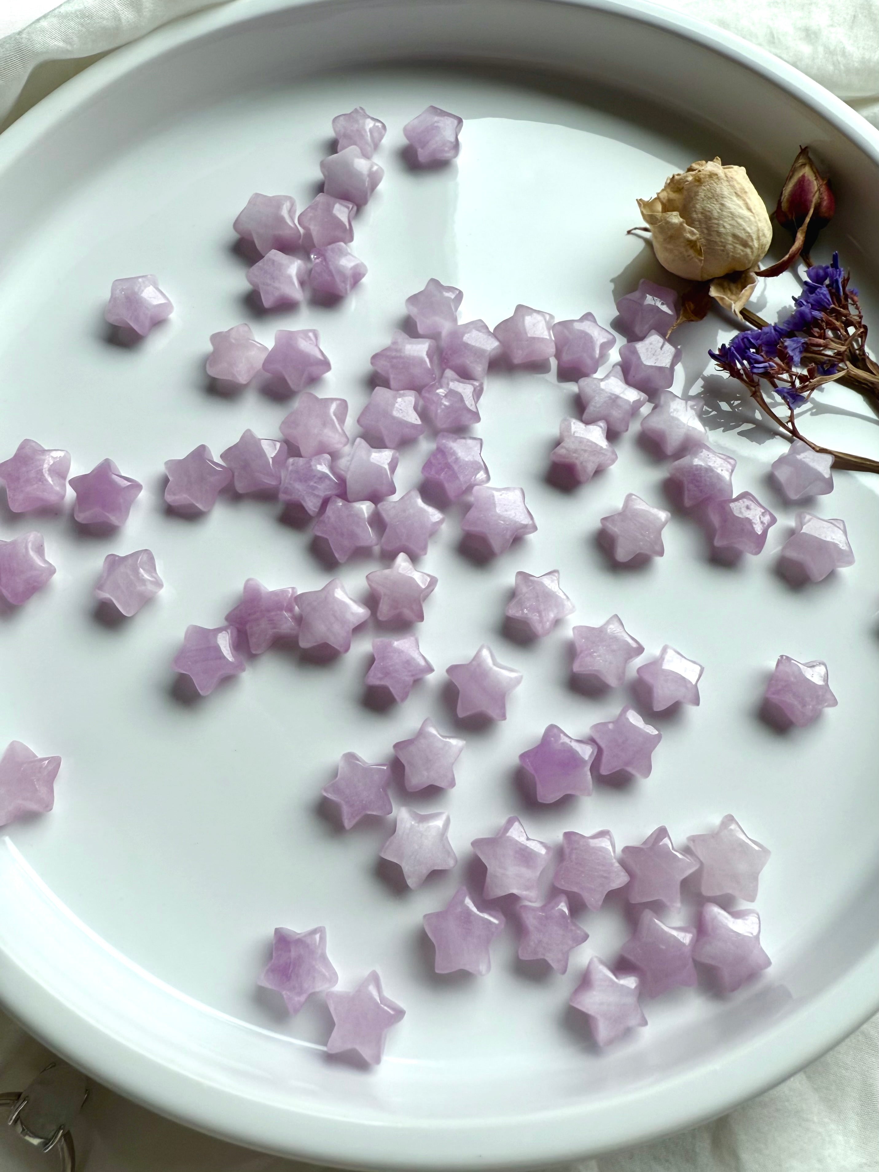 Dozens of glossy Kunzite stars on a white surface, tiny polished carvings for emotional healing and sacred rituals.