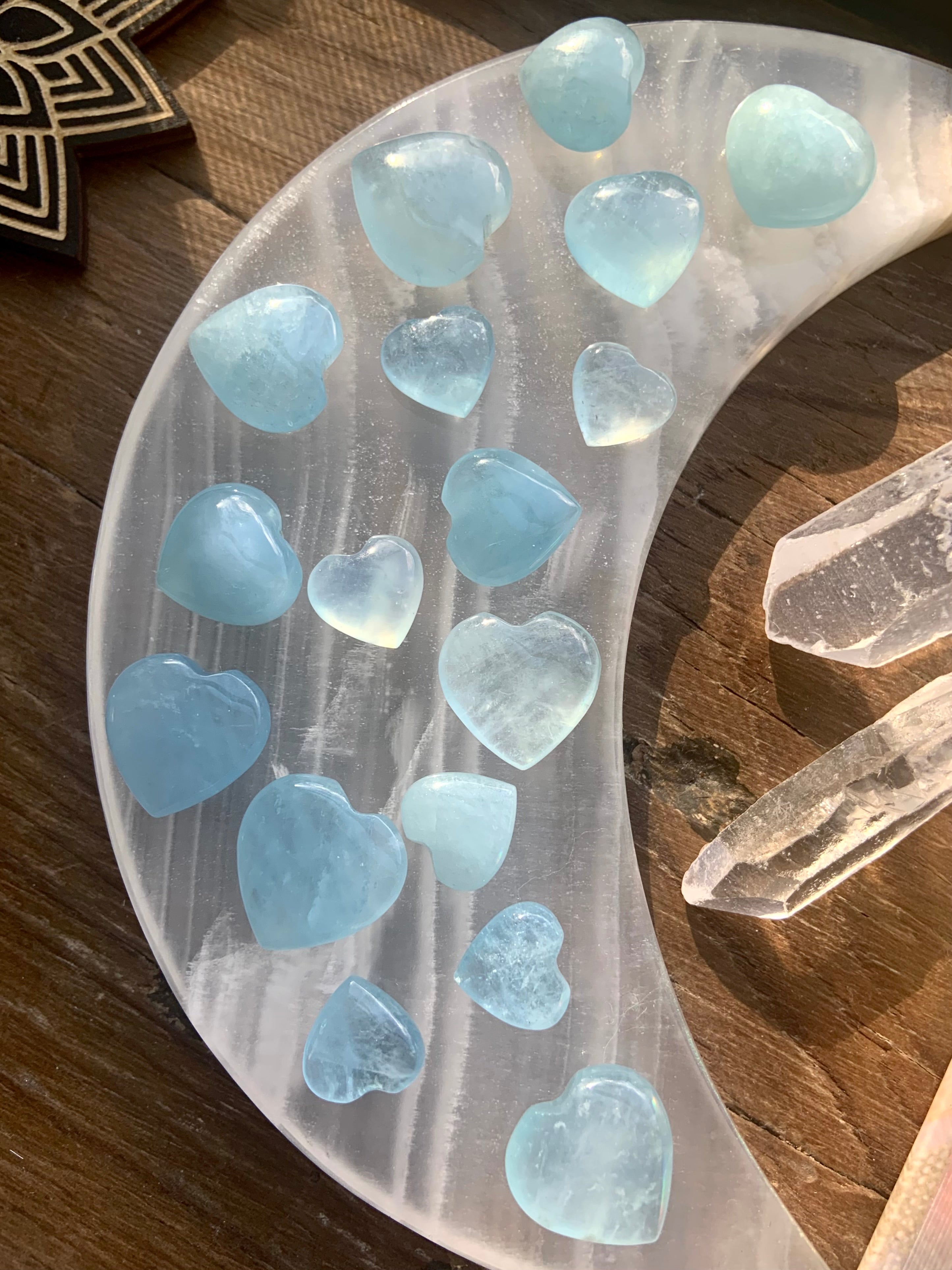 Overhead view of luminous Aquamarine crystal hearts arranged on a white stone moon plate with quartz points — soothing blue healing stones for calm + clarity.