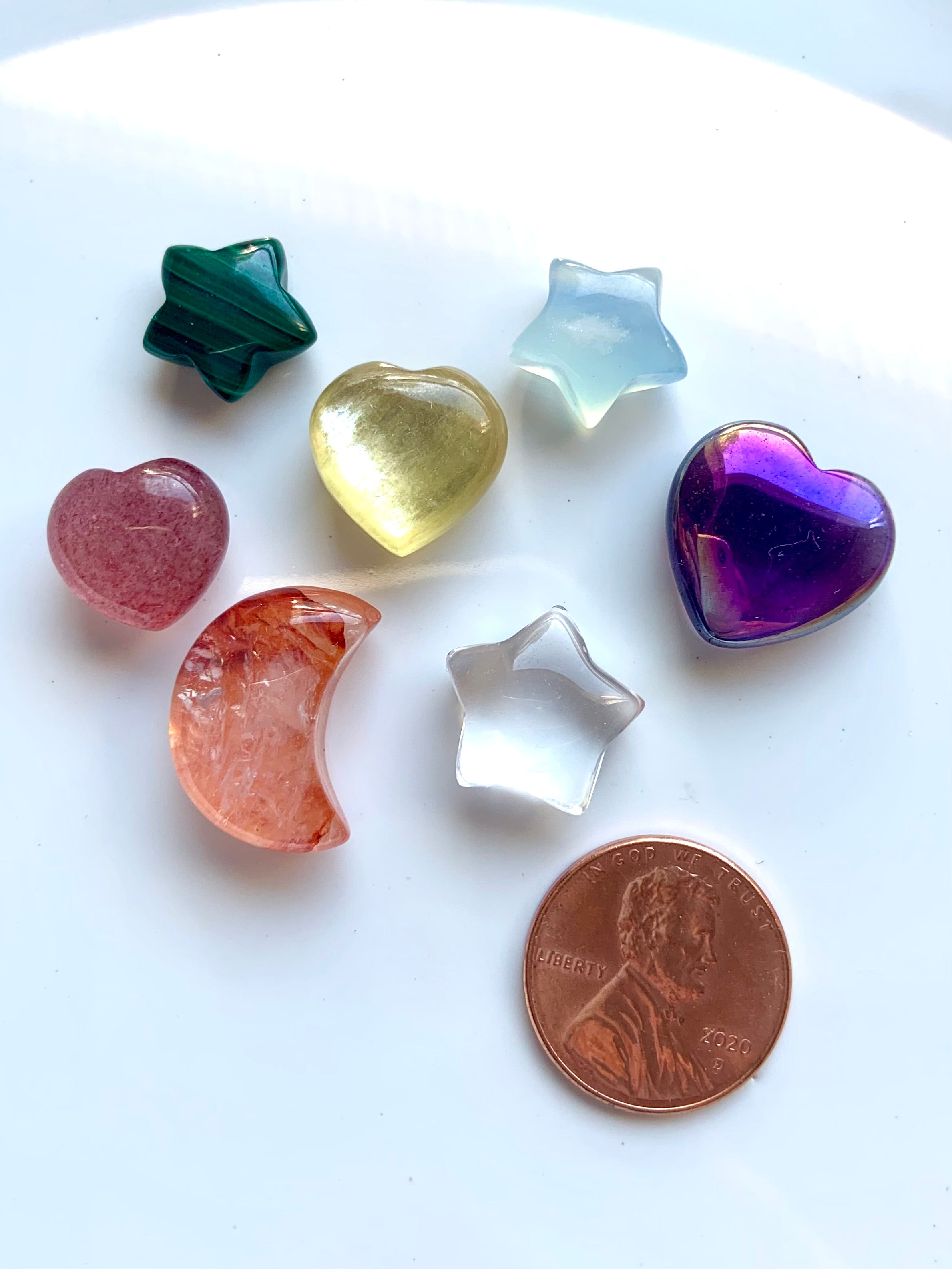 7 mini carved chakra crystals — hearts, stars & moon — shown with a penny for size comparison