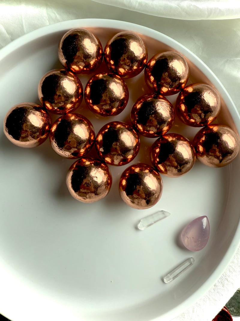 a white plate filled with small native copper spheres showing the glowing natural copper color