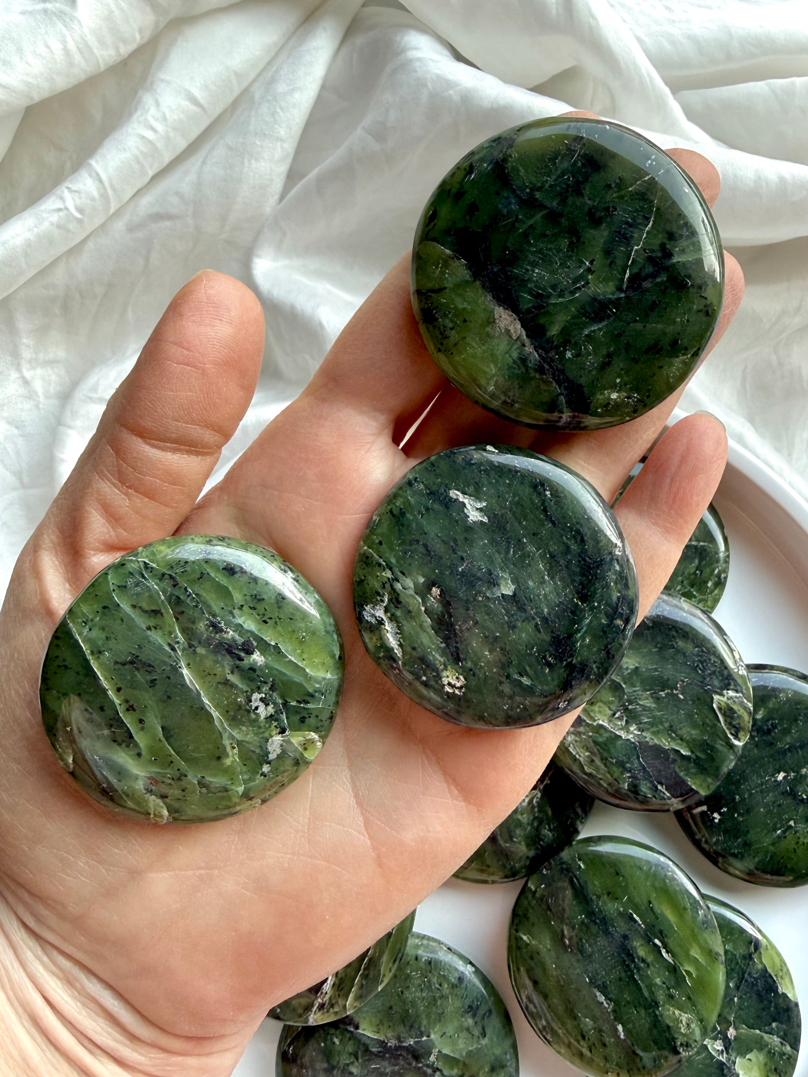 Three nephrite jade palm stones in hand showing smooth polished surface and deep green variations, heart chakra meditation crystals