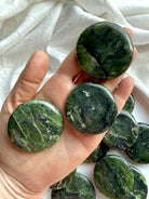 Three nephrite jade palm stones in hand showing smooth polished surface and deep green variations, heart chakra meditation crystals