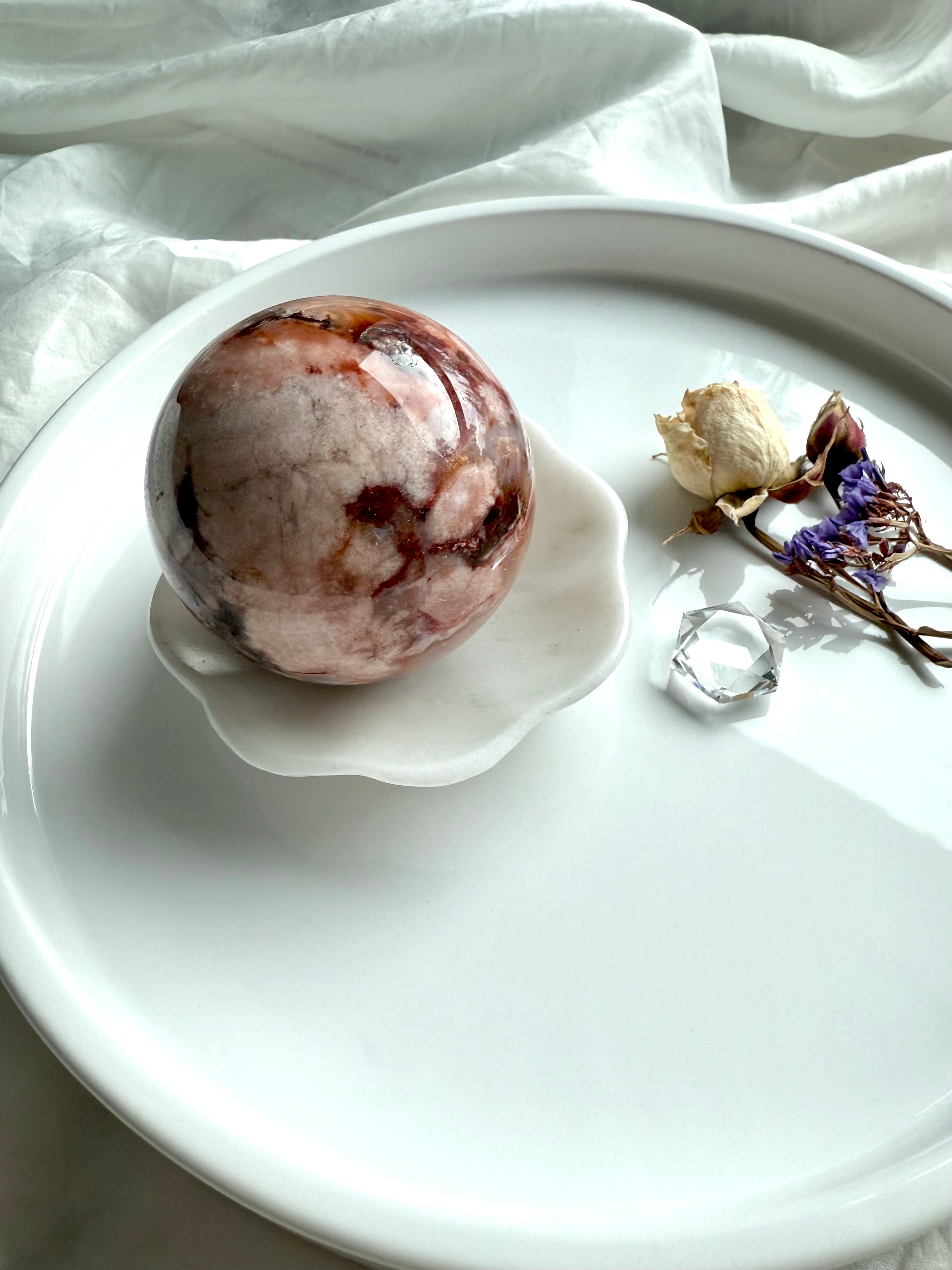 White marble daisy bowl holding a 56mm polished crystal sphere for display, styled with dried flowers and a clear quartz hexagon 