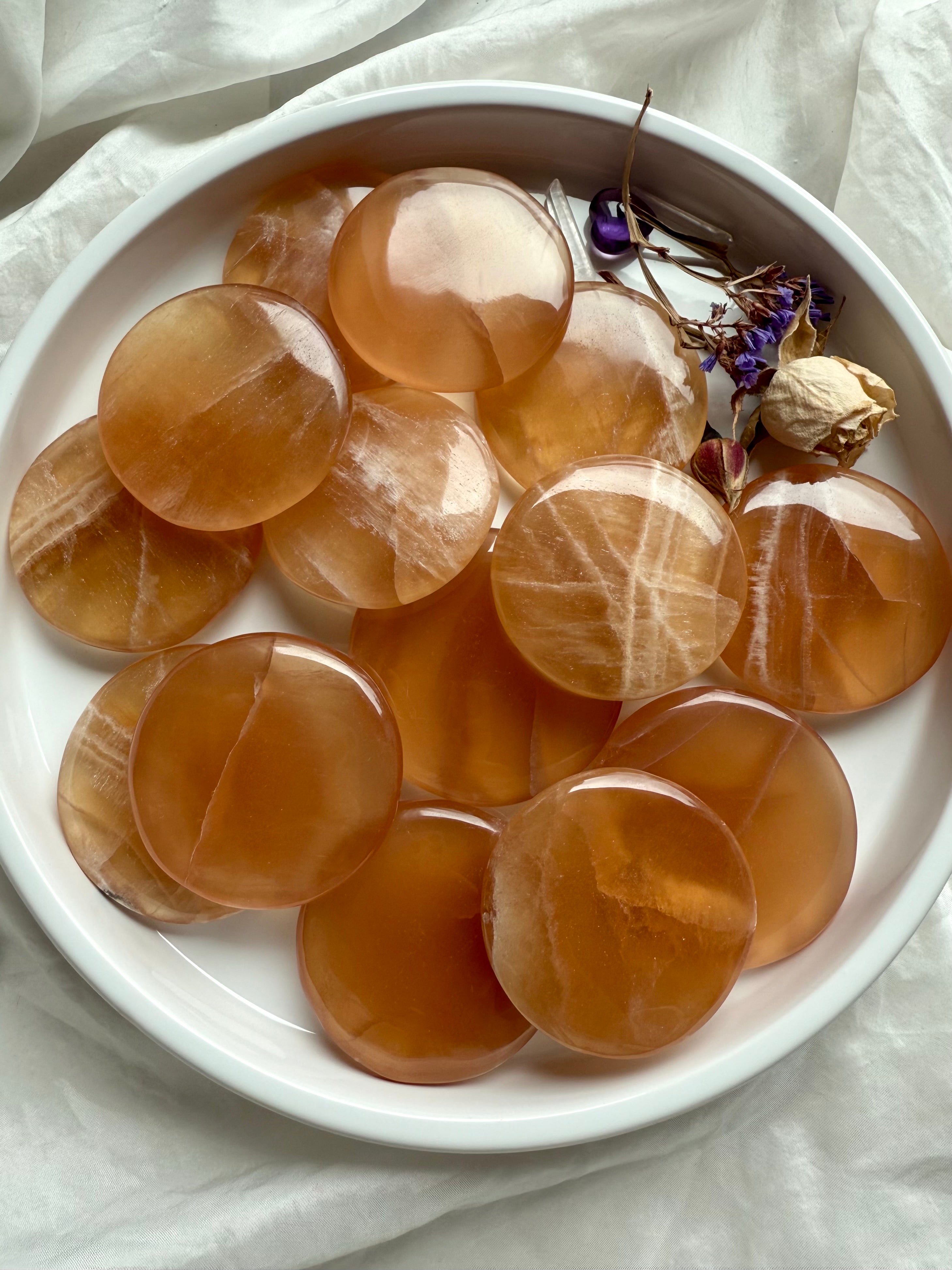Polished honey calcite meditation stones in a white ceramic bowl with dried flowers, ideal for energy work and Solar Plexus chakra healing.