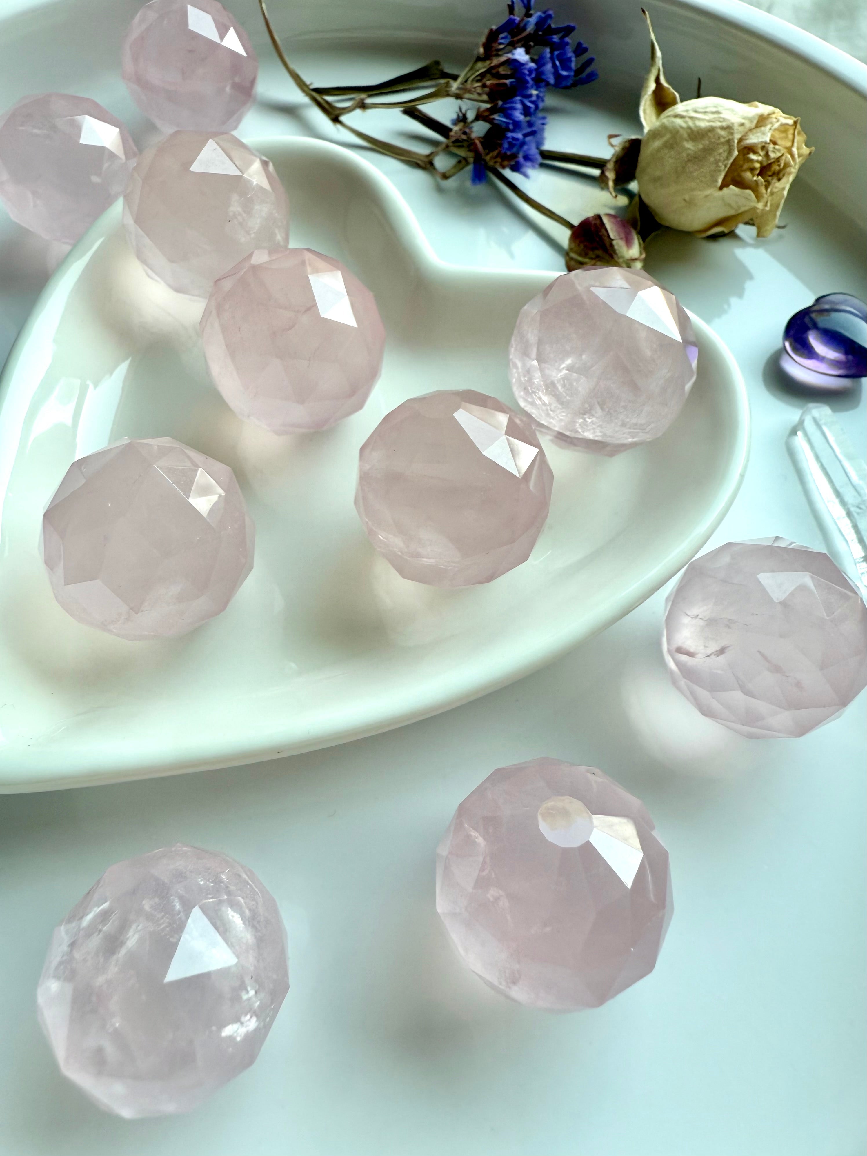 Faceted pink crystals on a white plate with dried flowers. Heart chakra stones for unconditional love.