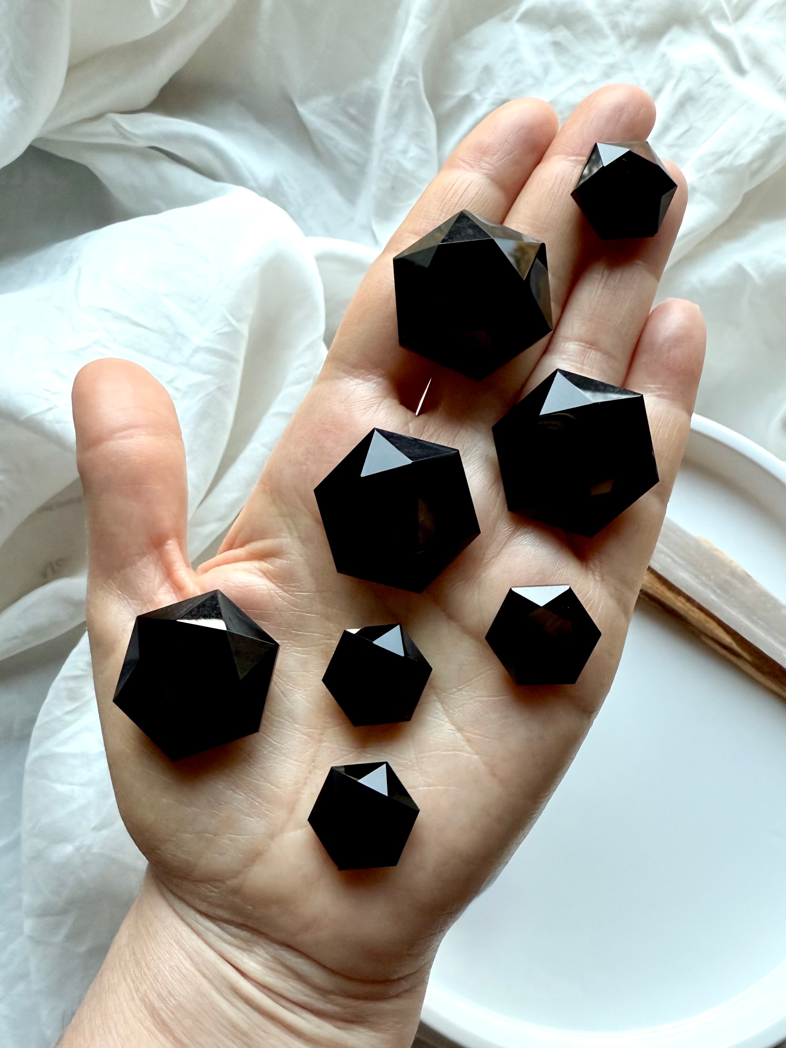 Array of faceted Black Obsidian hexagon crystals resting in an open palm, showcasing glossy reflective facets and Root Chakra protection energy