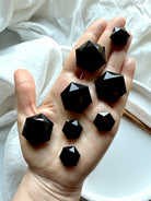 Array of faceted Black Obsidian hexagon crystals resting in an open palm, showcasing glossy reflective facets and Root Chakra protection energy