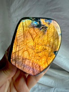 Orange Flash Labradorite freeform held in sunlight showing vibrant coppery orange and purple color play