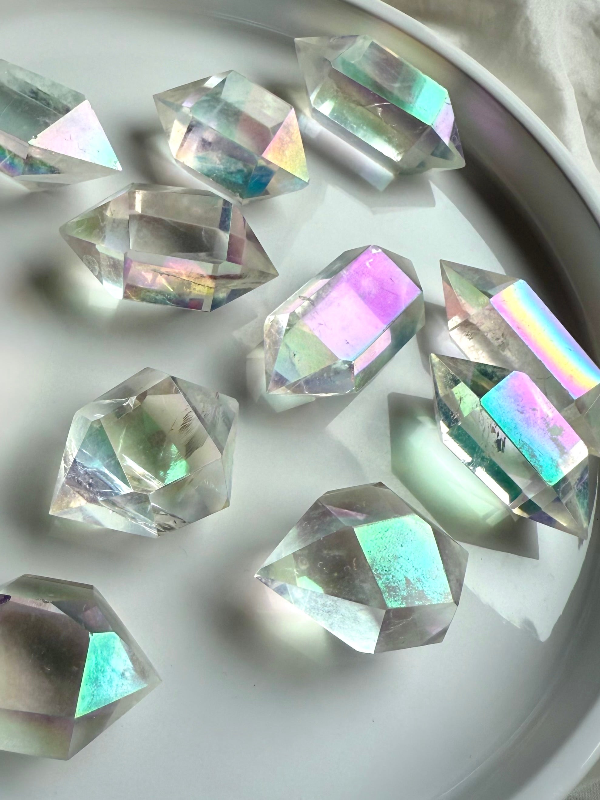 Angel Aura Quartz double terminated points in a circular display dish, glowing with rainbow light for moon rituals and altar décor