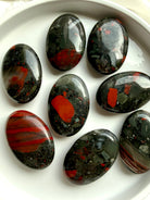 Bloodstone palm stones arranged together showing natural variation in red banding, green matrix and mineral inclusions