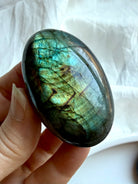 Green flash Labradorite palm stone held in hand with vibrant labradorescence and natural mineral patterns