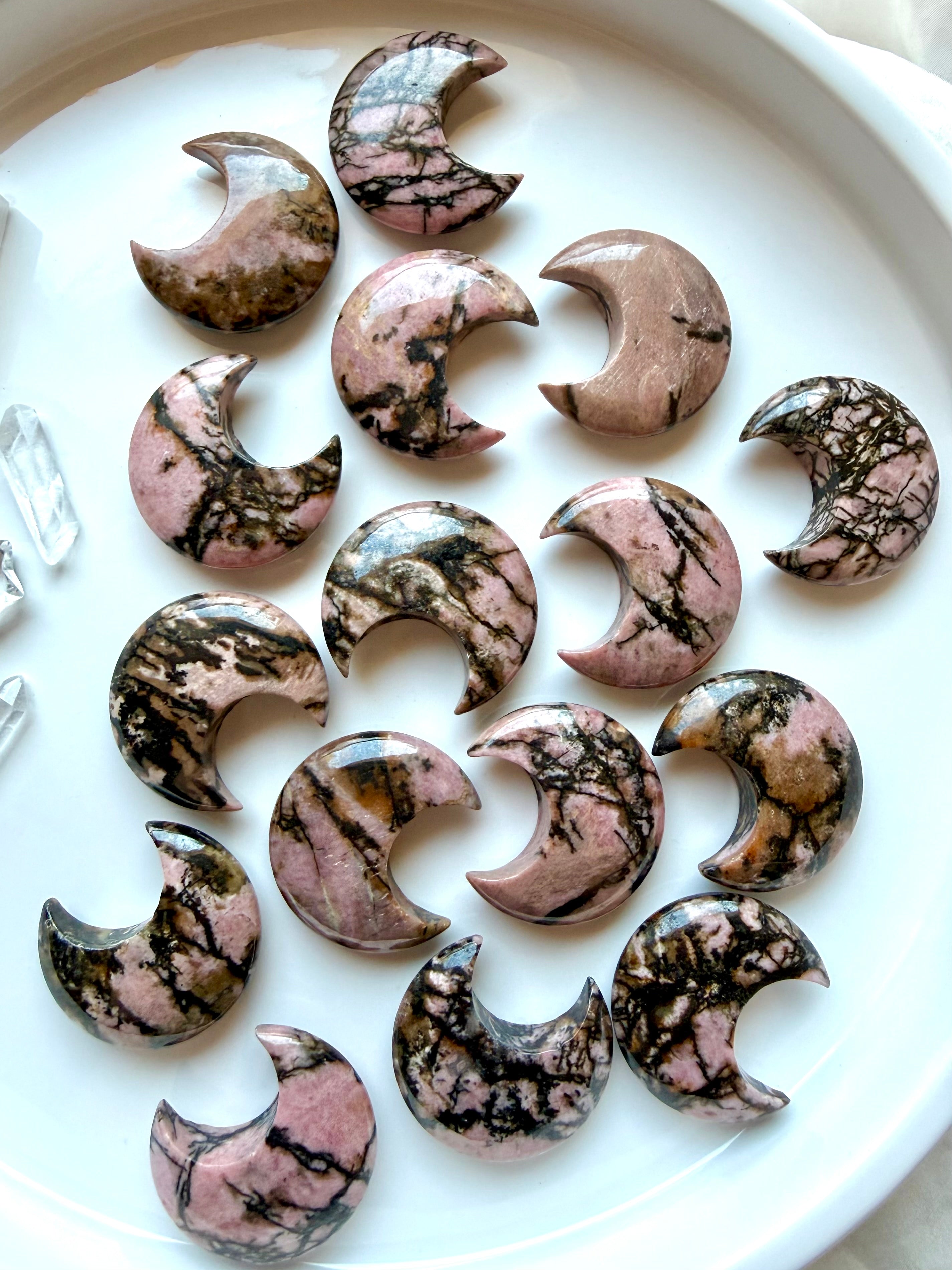 Polished Rhodonite crescent moon crystals displayed together with natural pink, black and earthy mineral veining