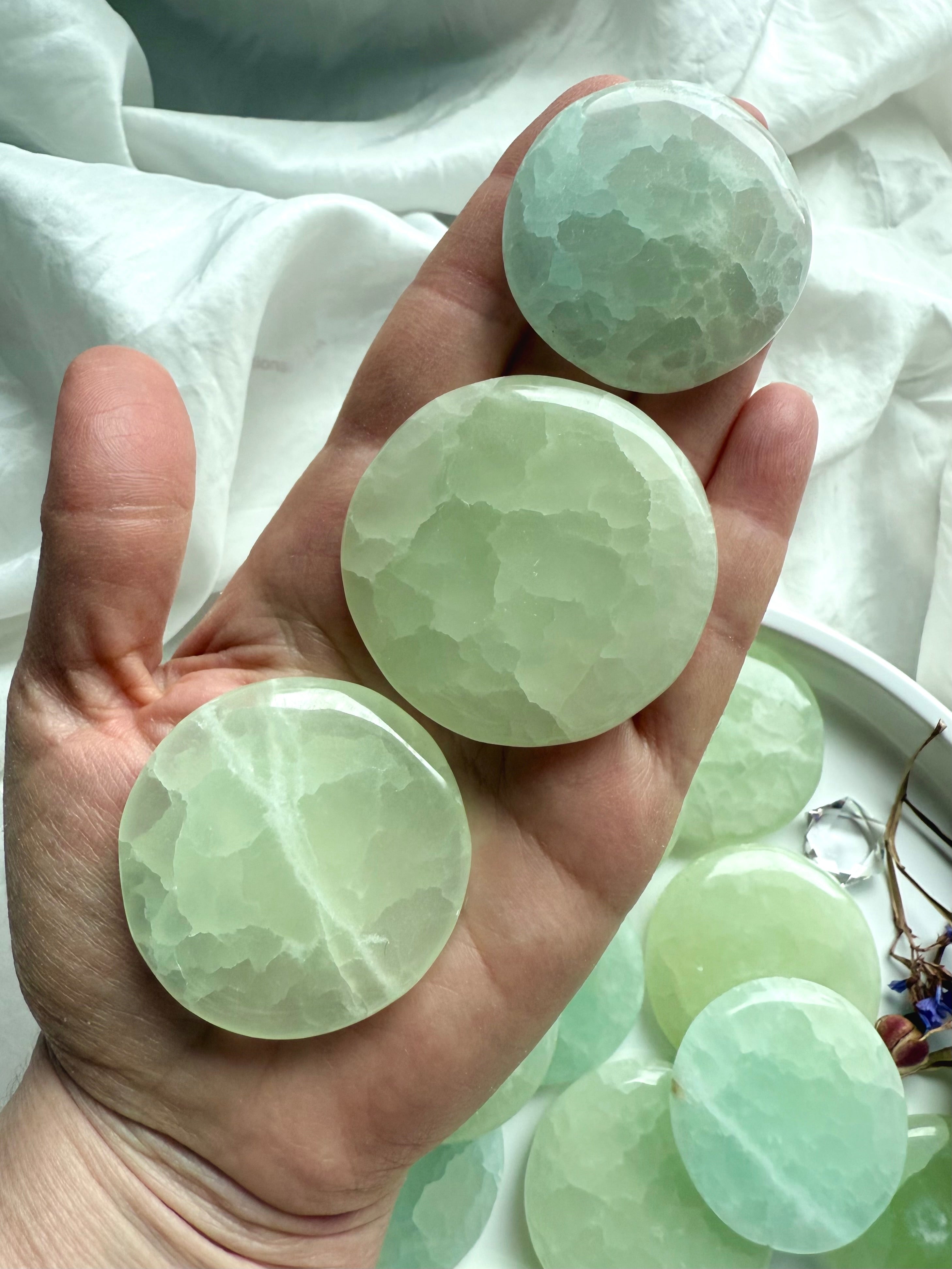 Hand holding three Pistachio Calcite palm stones to show size and color variation – seafoam green healing crystals for chakra work