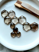 Collection of smoky quartz hexagons arranged in a honeycomb pattern on a white tray with palo santo and selenite – Root Chakra crystals for ritual and energy work.