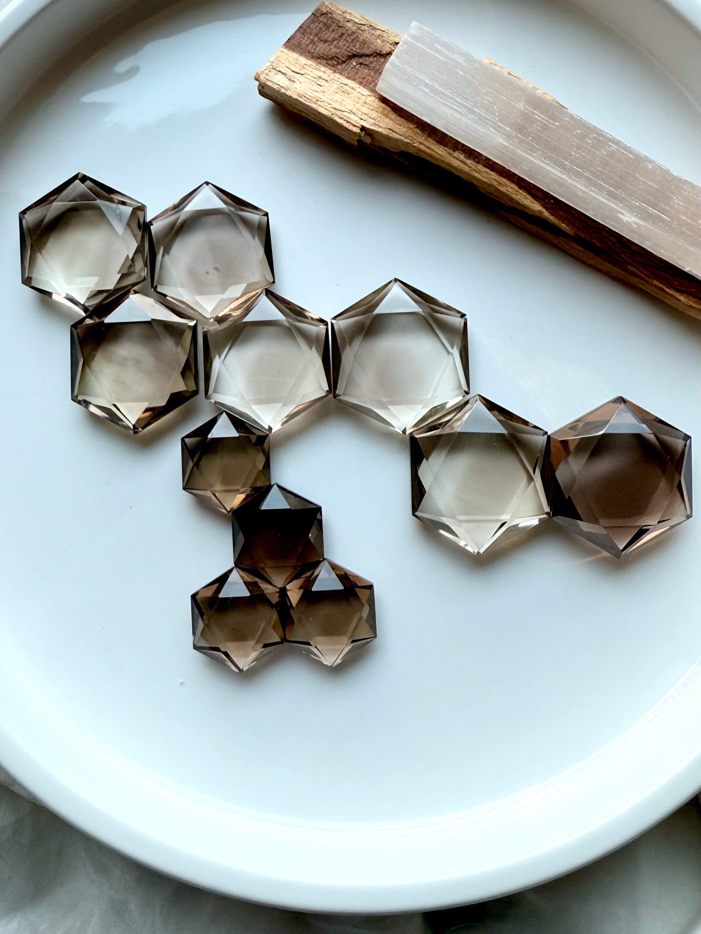 Collection of smoky quartz hexagons arranged in a honeycomb pattern on a white tray with palo santo and selenite – Root Chakra crystals for ritual and energy work.