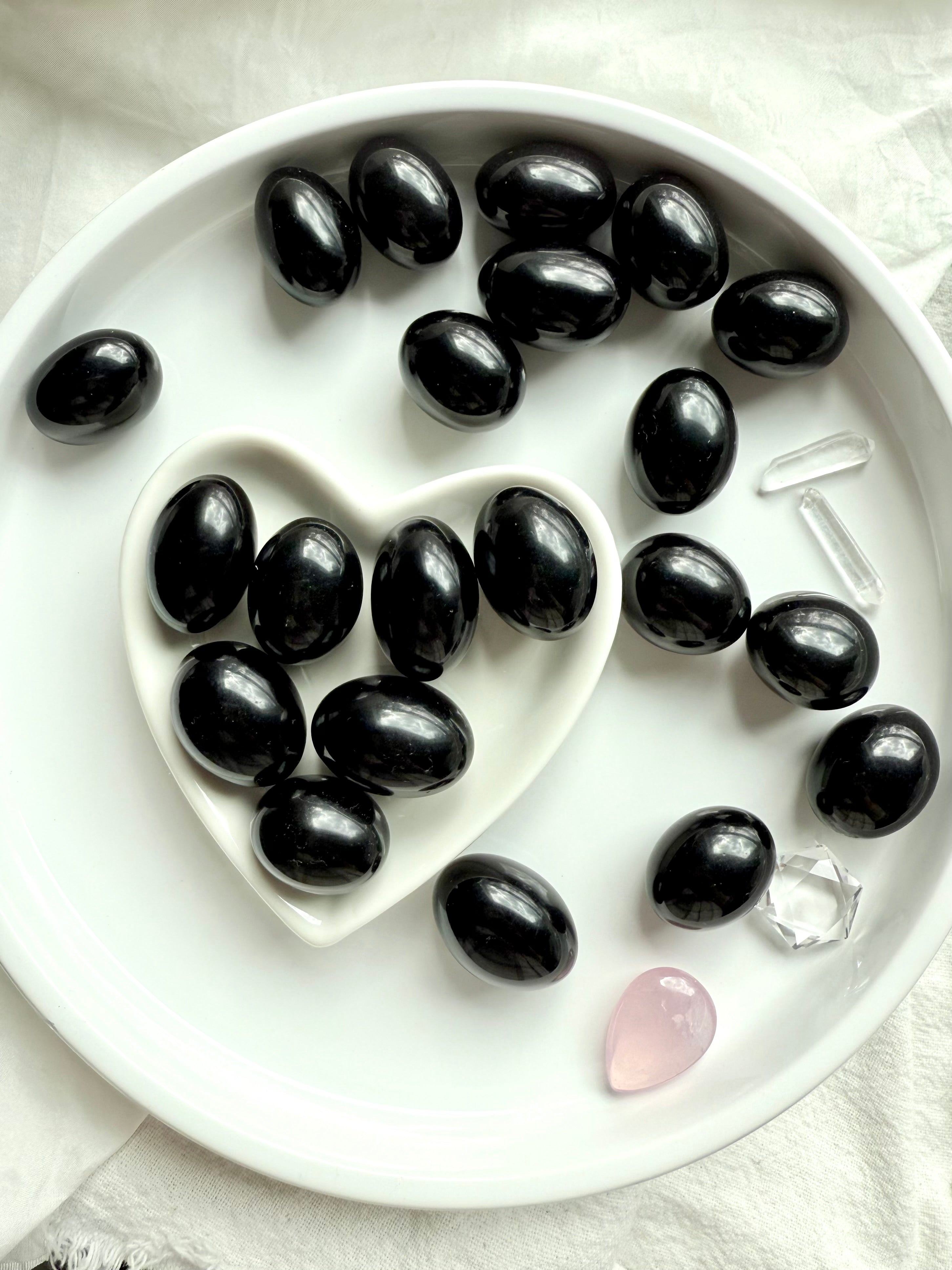An array of Black Obsidian Tumbles shown on a white plate, photographed in natural light