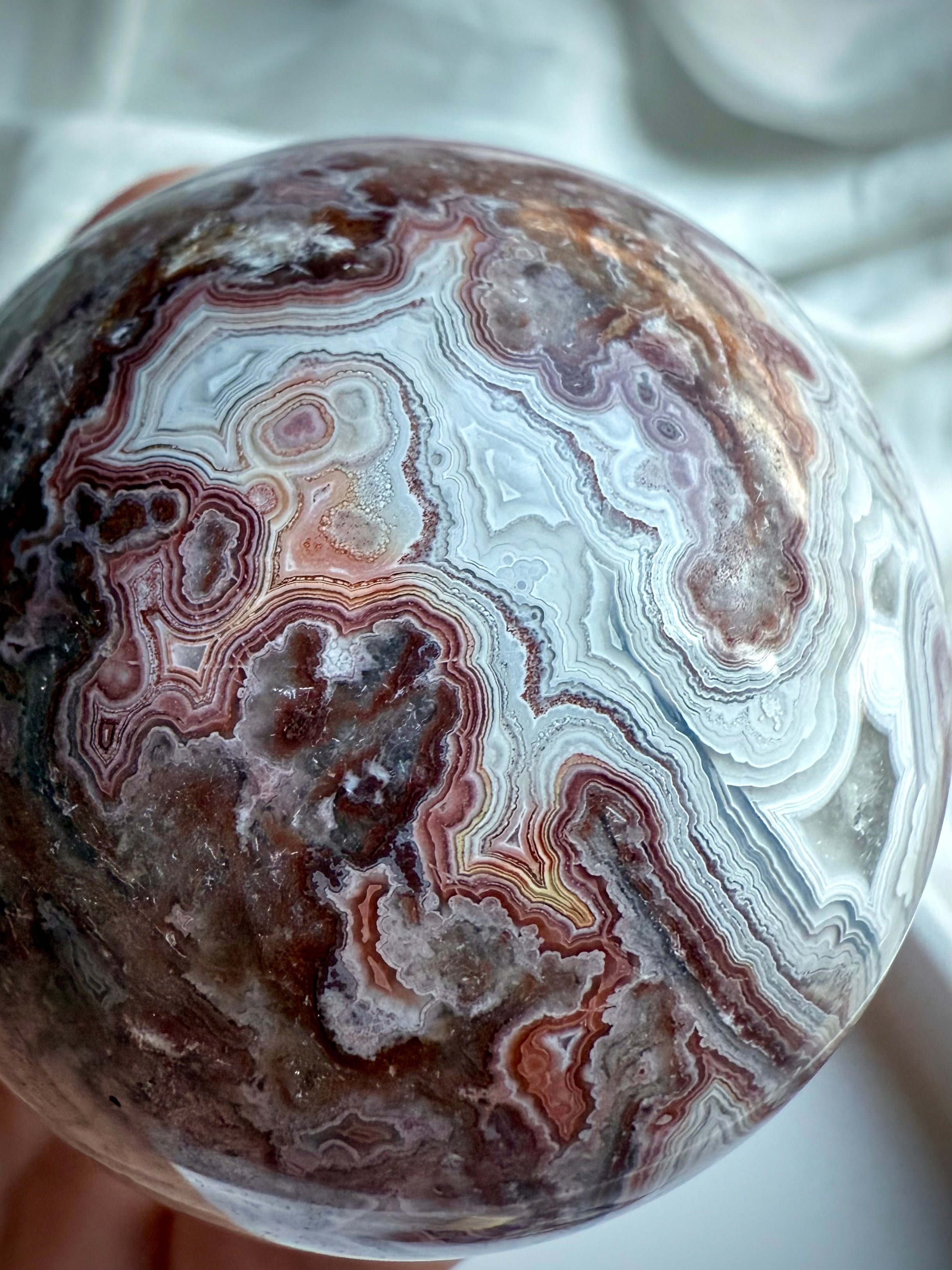 Crazy Lace Agate sphere featuring swirling lace-like patterns in earthy red, gray, and cream tones