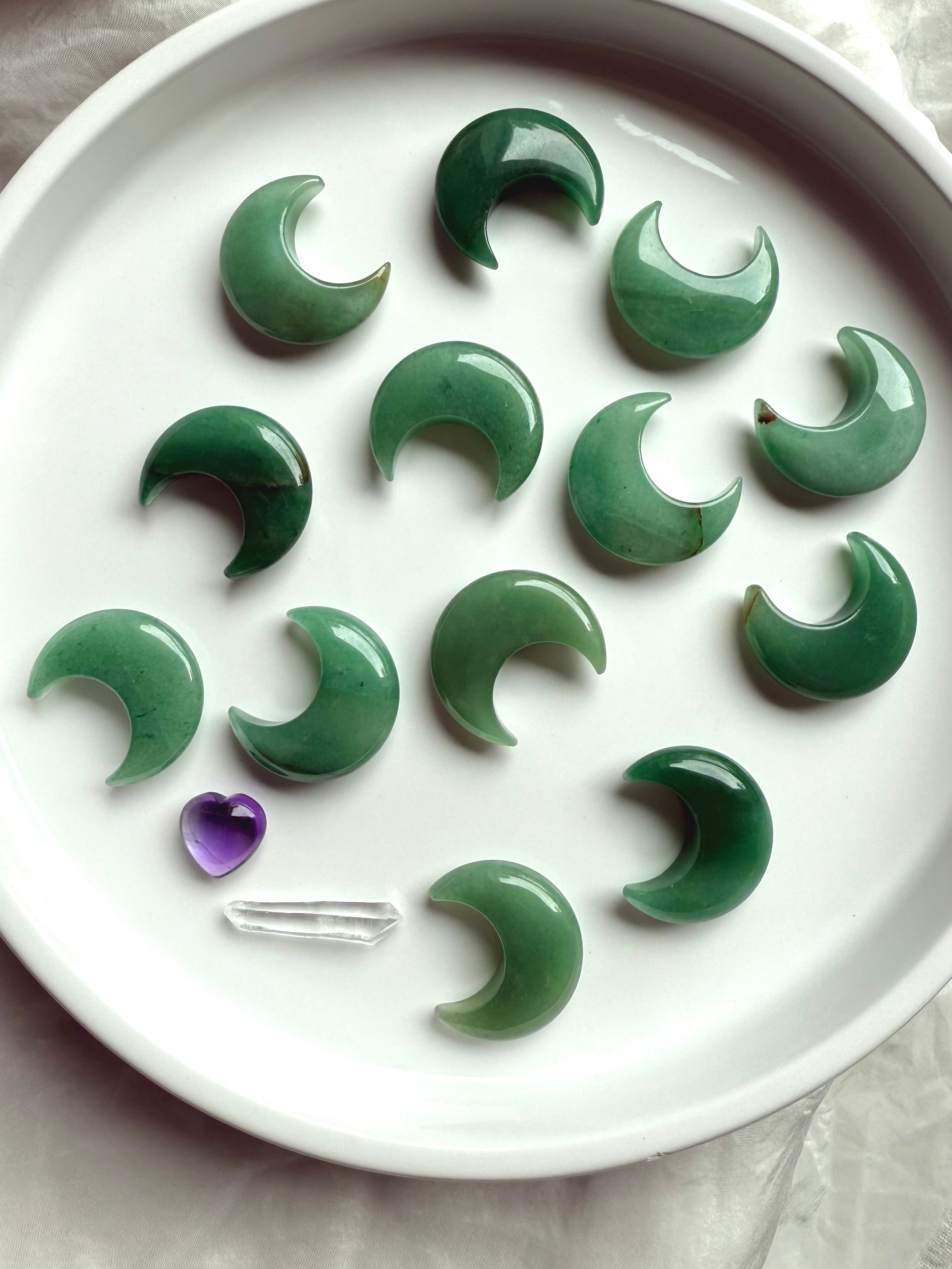 Flatlay of Green Aventurine crescent moons on a white plate with amethyst heart and clear quartz point, Heart Chakra crystal carvings for love and abundance