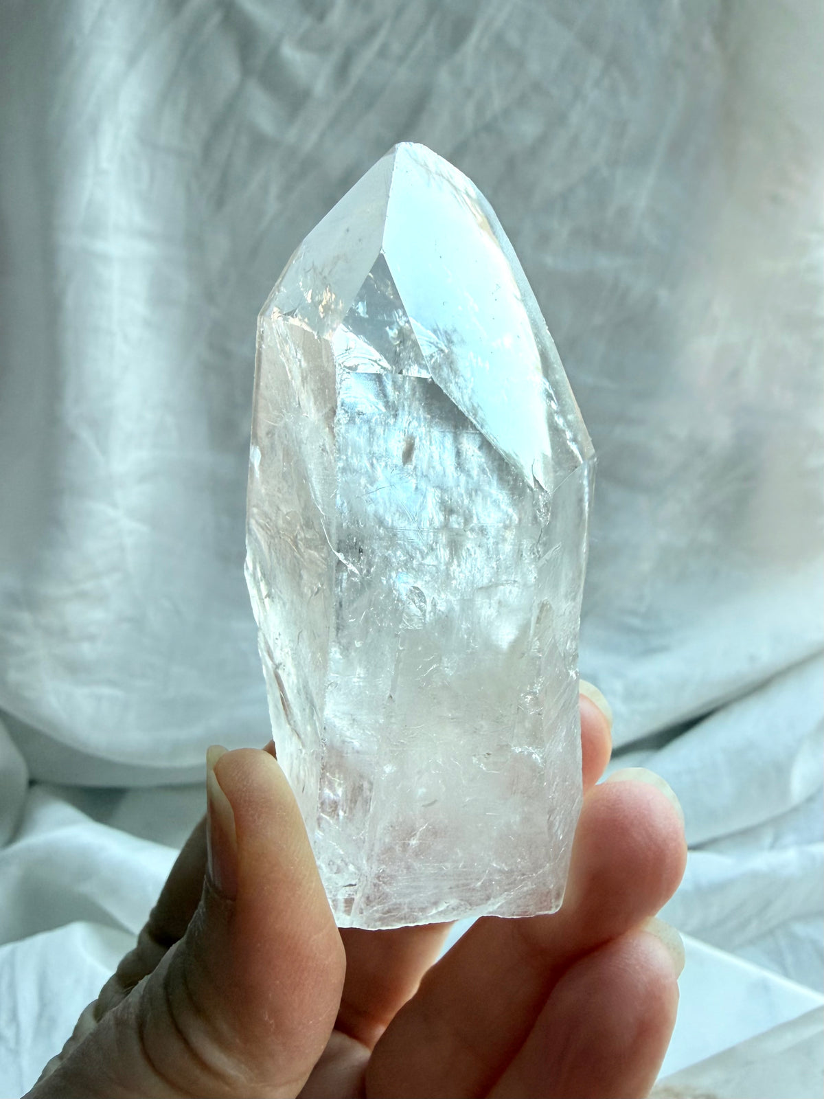 Brazilian Lemurian Quartz point held in hand with textured growth lines, cloudy veils, and a naturally formed termination
