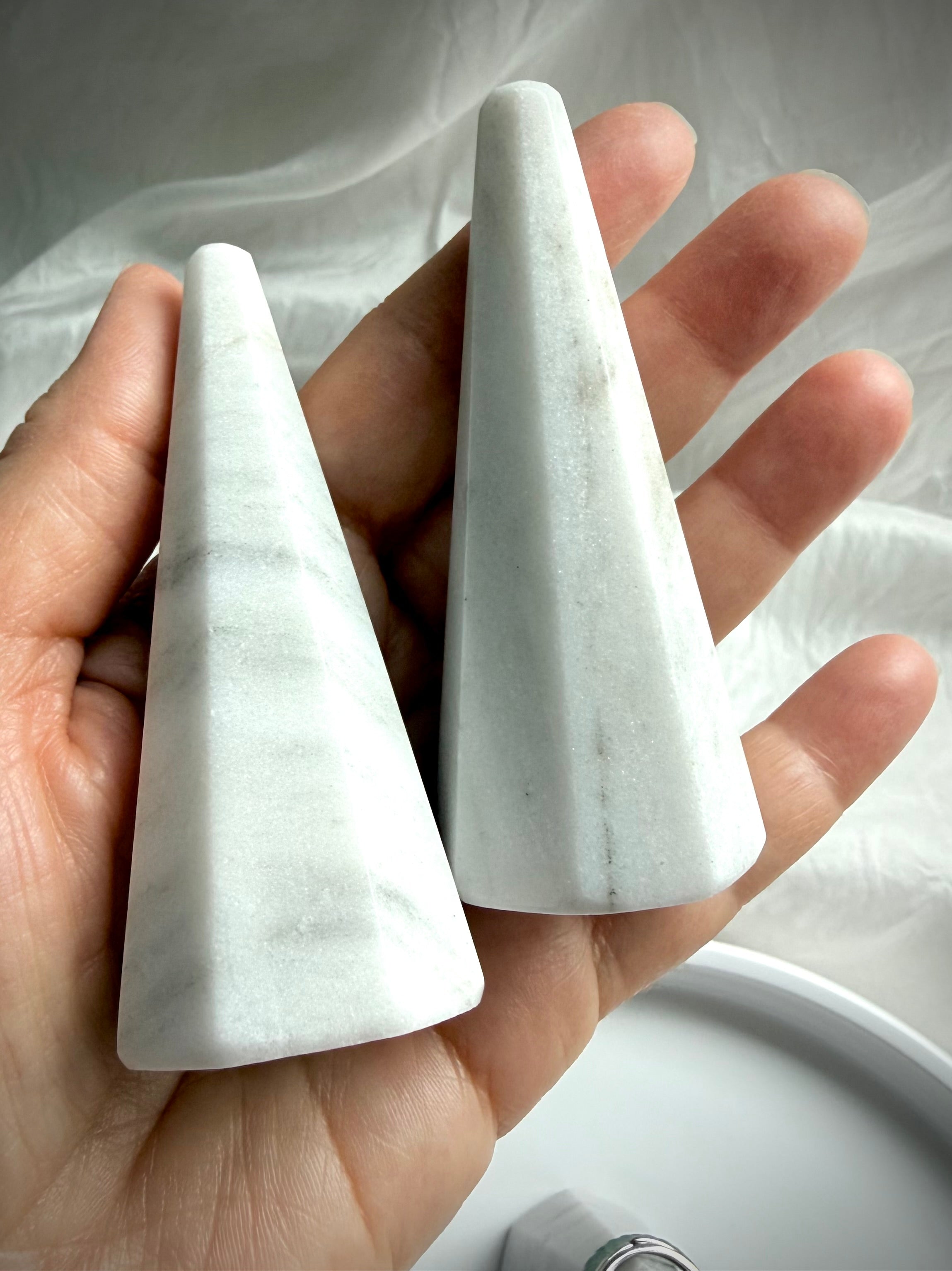 White and gray marble ring holder stand held in hand showing faceted beveled edges and natural veining