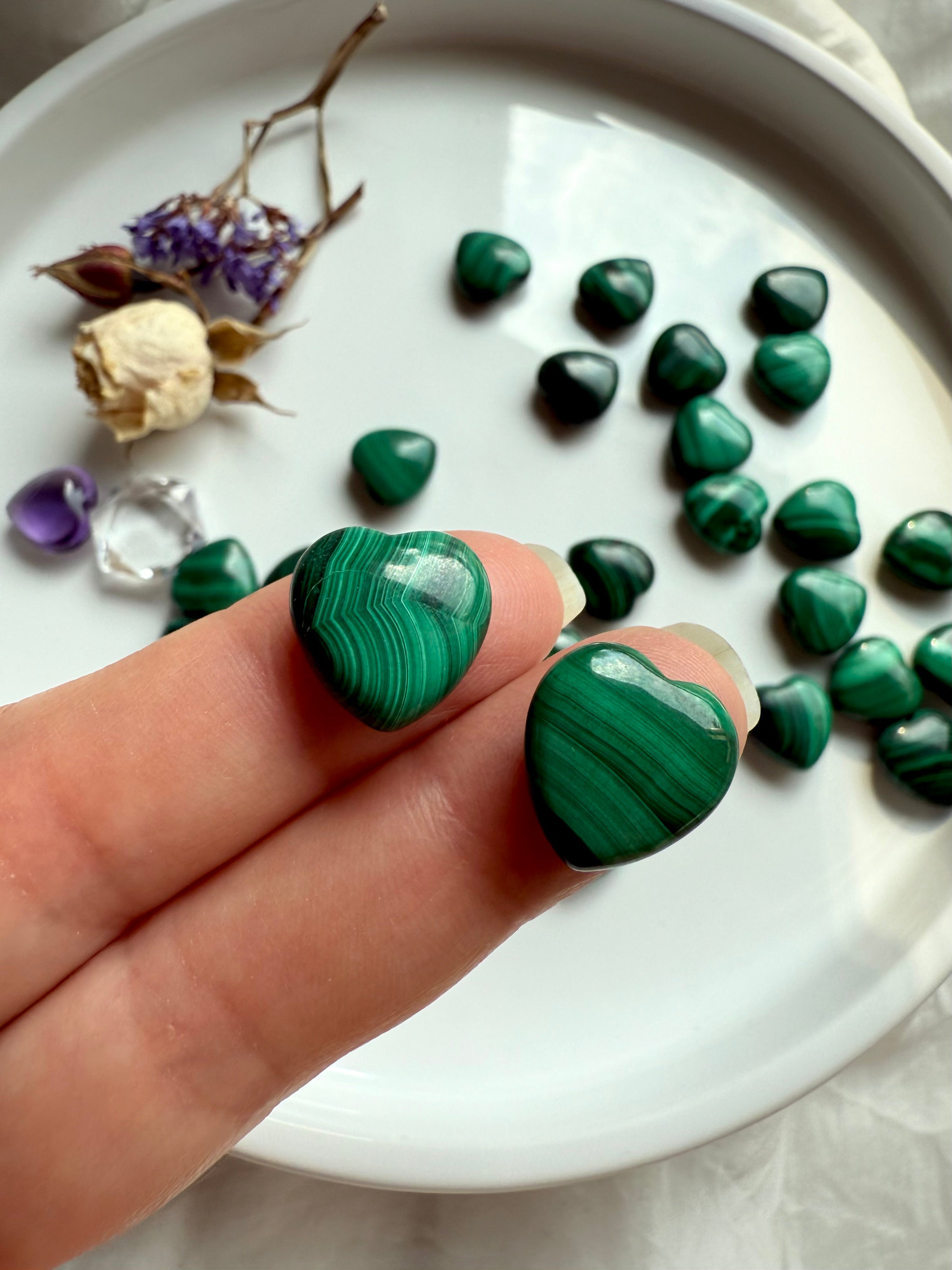 Two Malachite mini heart carvings held on my fingertips to show size and pattern detail.