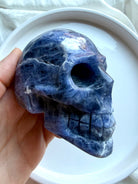 Polished Sodalite skull carving held in hand showing size, detailed carving, and natural blue stone