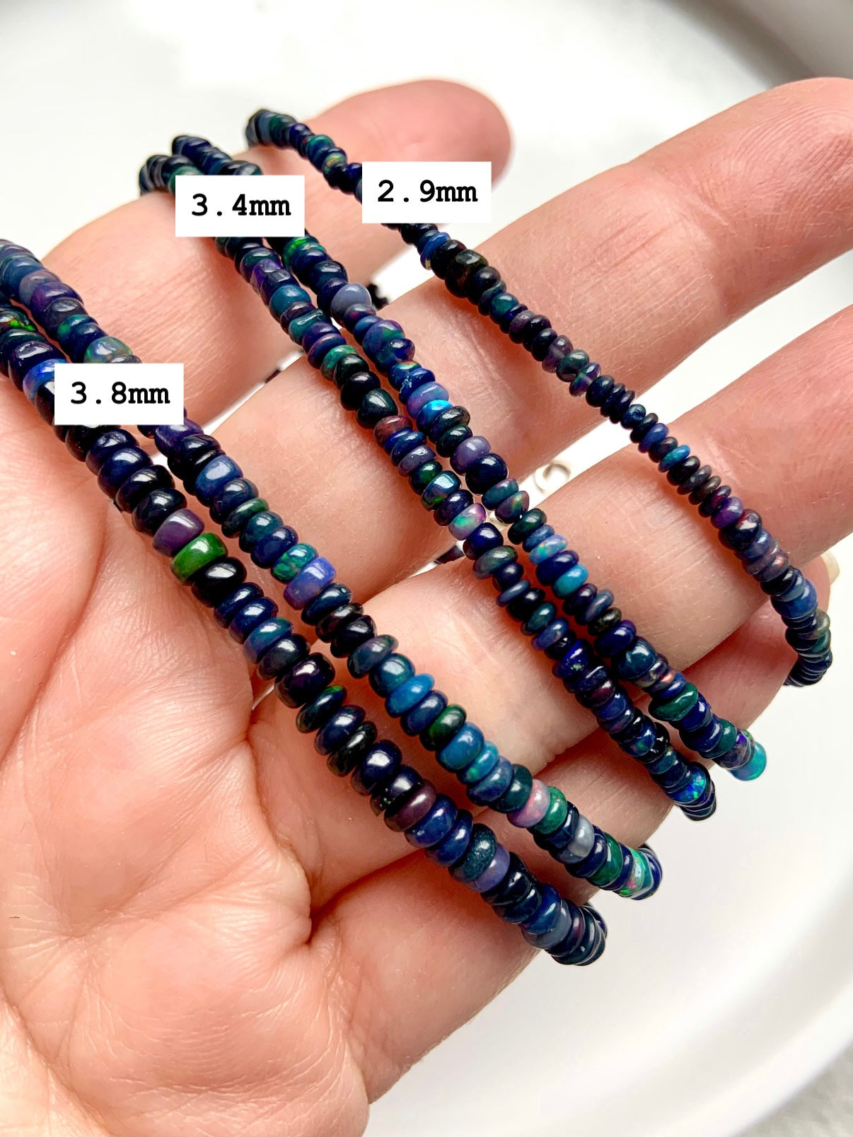Three Black Fire Opal bracelets in bead sizes 2.9mm, 3.4mm, and 3.8mm displayed over a hand — size guide for opal bead jewelry.