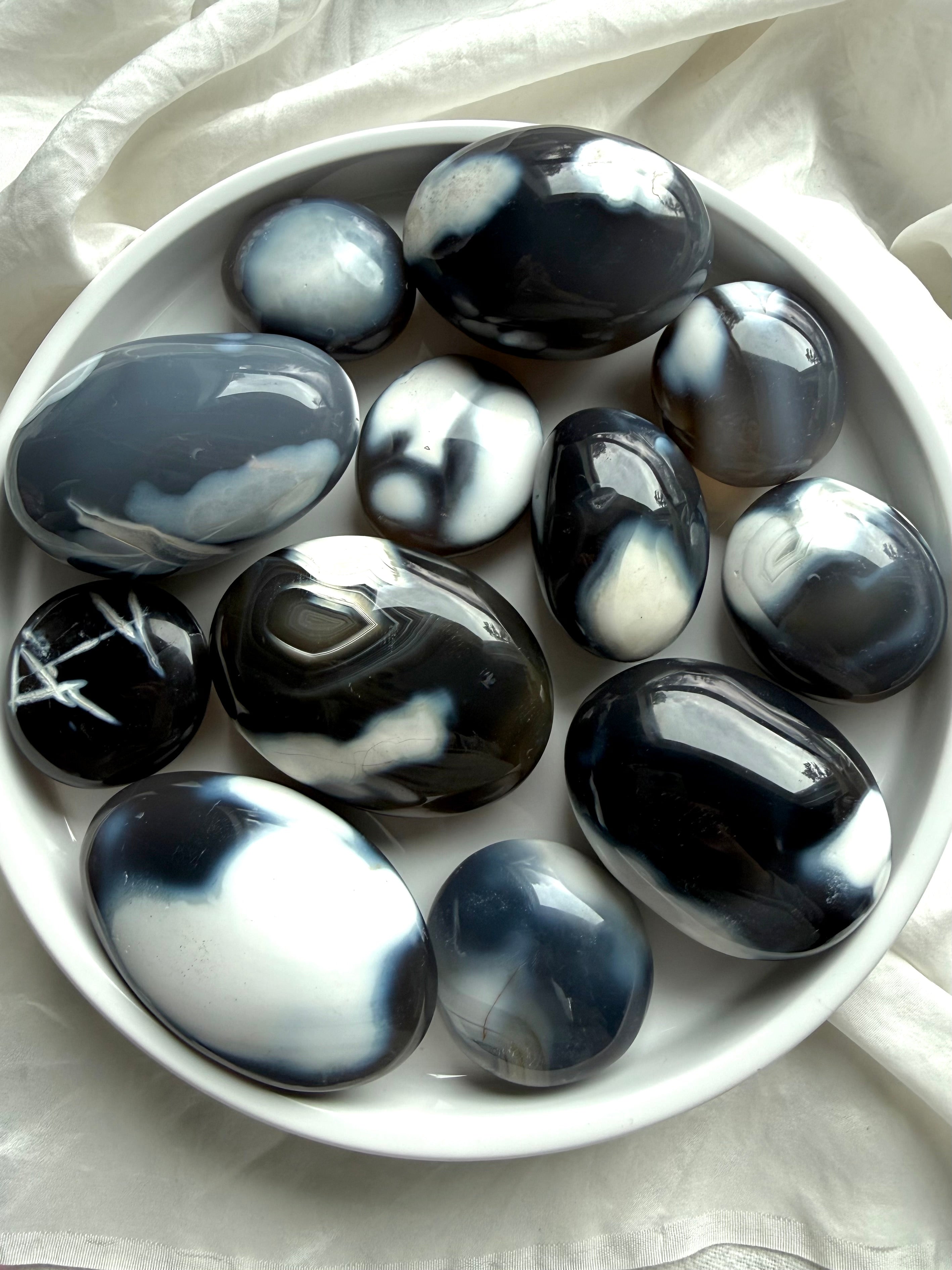 Collection of polished Orca Agate palm stones in a white bowl, showcasing natural banding and soothing ocean-inspired tones