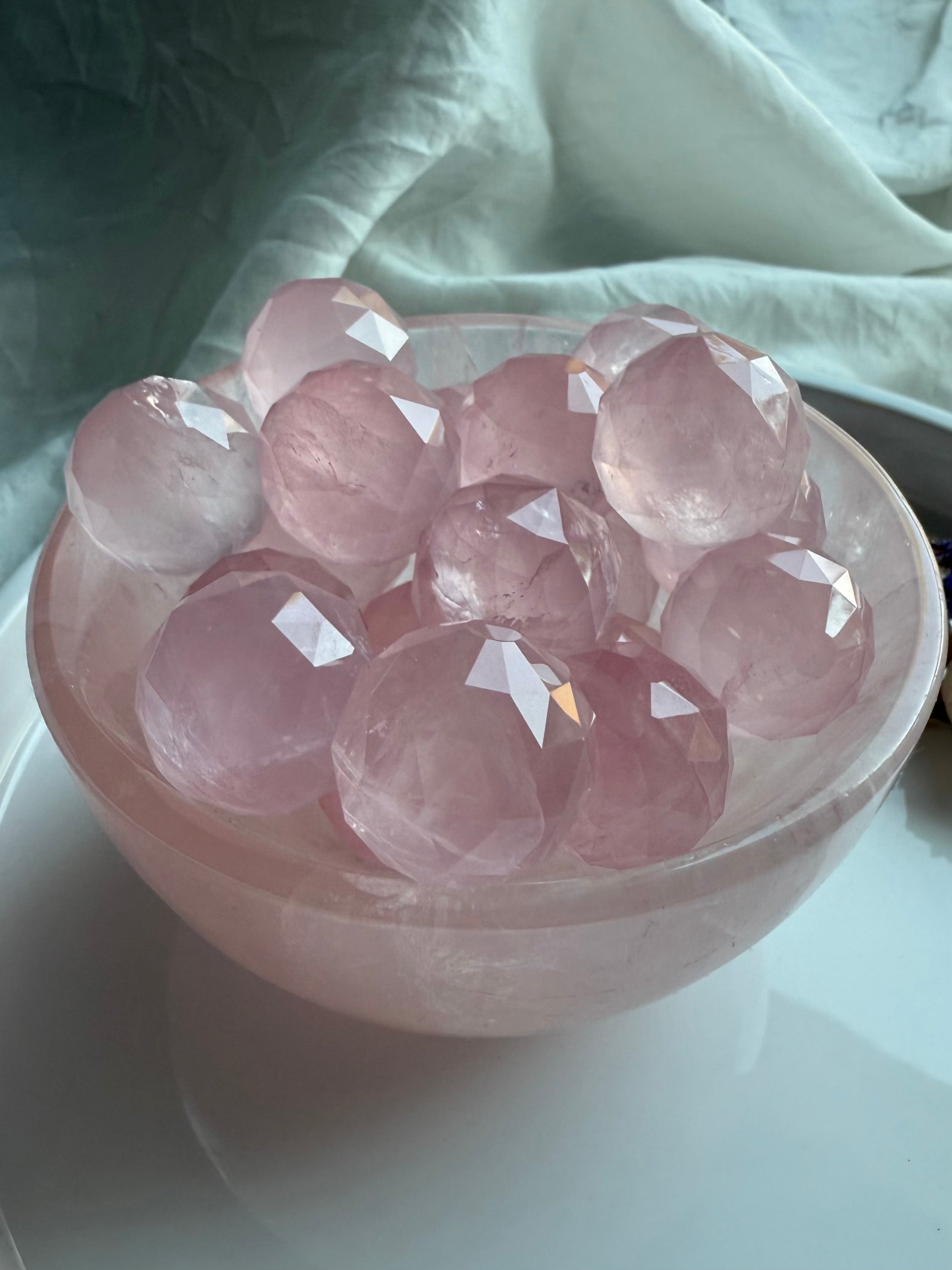 Glowing pink crystal balls in a rose quartz crystal bowl on a white surface. Calming crystals for peace.