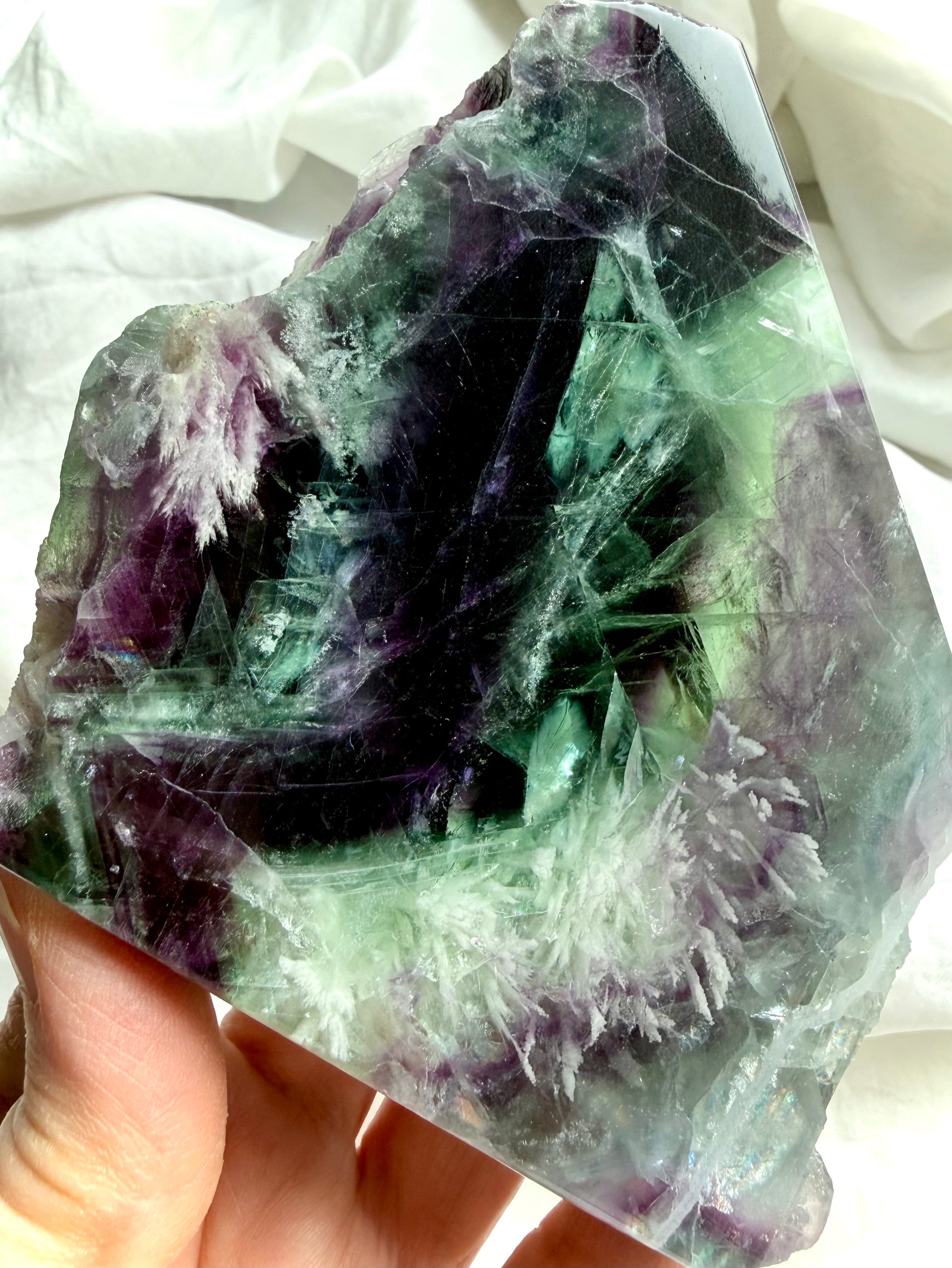Polished fluorite slab photographed in natural light highlighting layered green and violet color zoning with rainbows