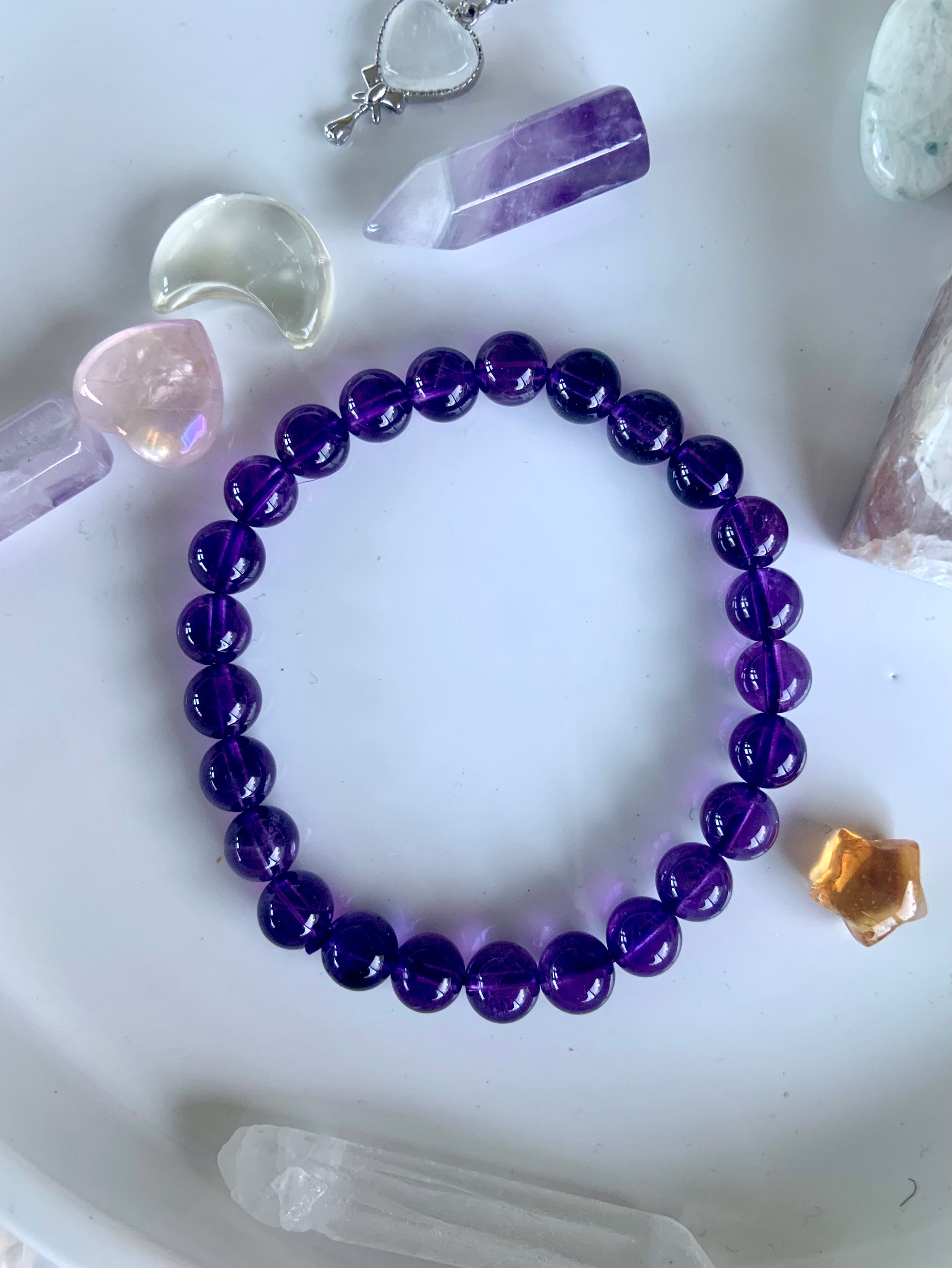 Overhead view of a deep purple amethyst crystal bracelet on a white plate with mini crystals in the background