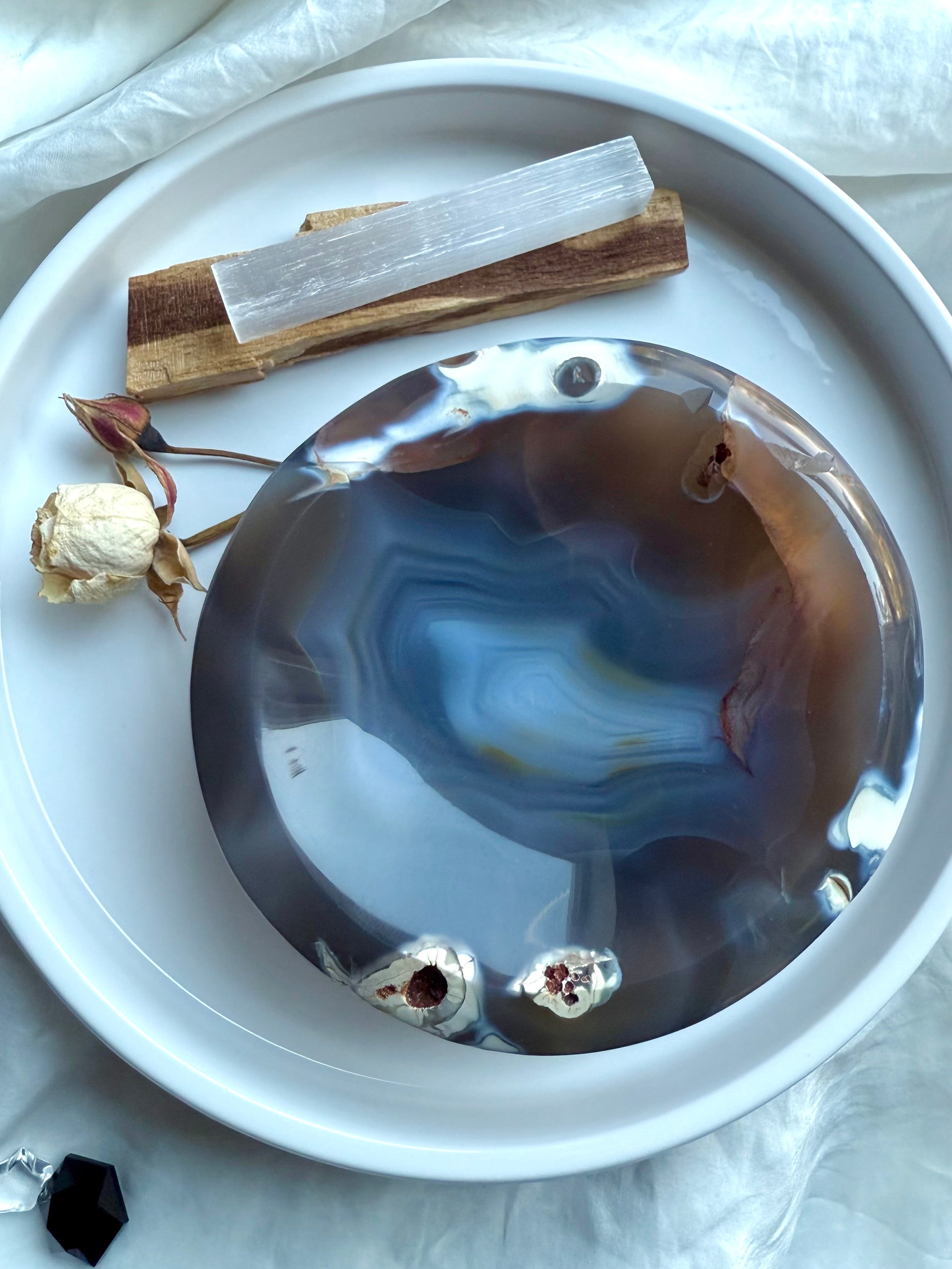 Orca Agate crystal bowl on white tray with selenite stick, palo santo, and dried flowers for cleansing rituals
