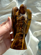 Front view of Golden Tiger’s Eye angel sculpture held in hand against soft white background